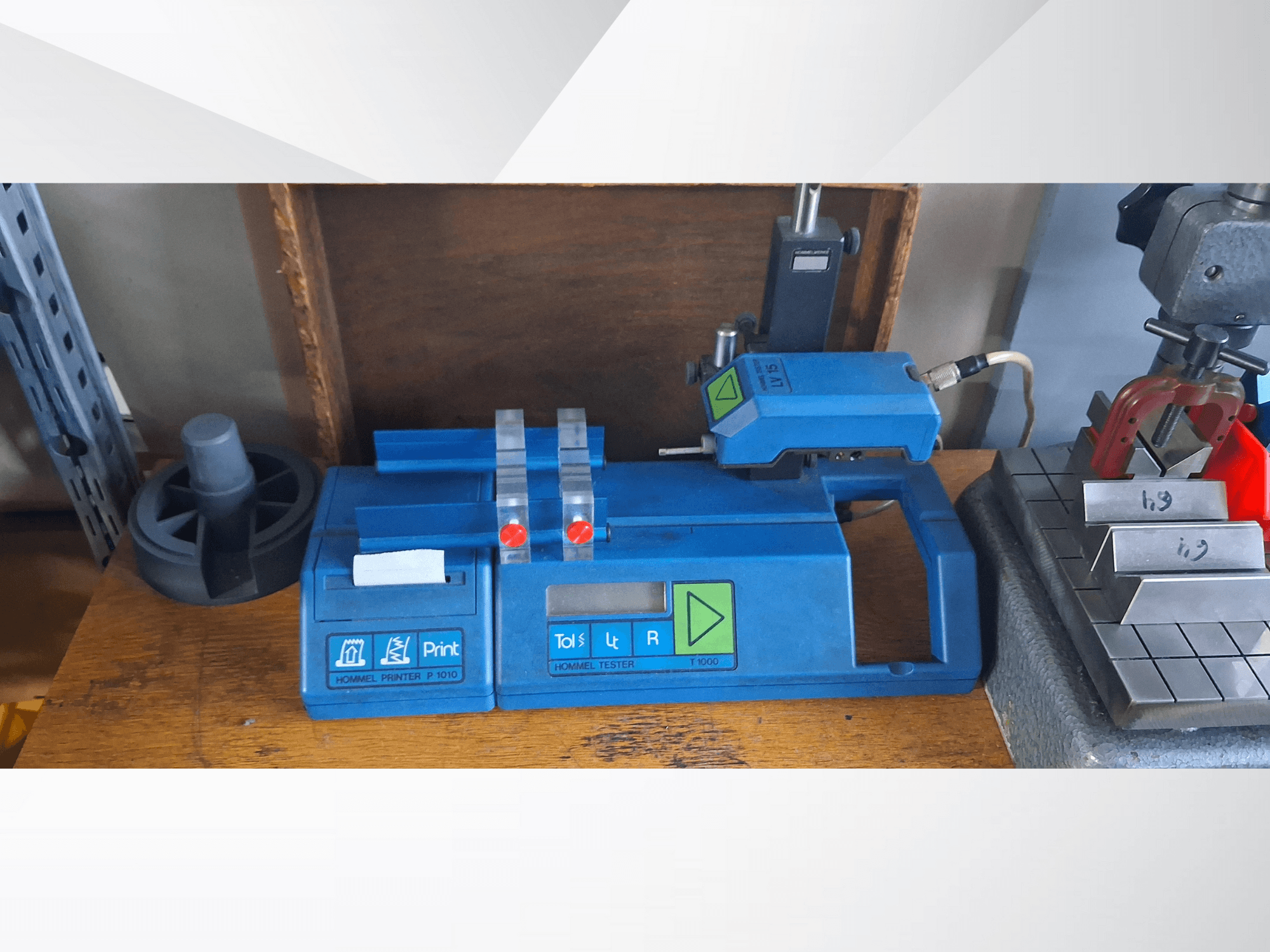 Tiskárna Hommel P 1010 a tester T1000 v bočním pohledu, s modrým krytem, tlačítky a červenými indikátory, na pracovním stole.