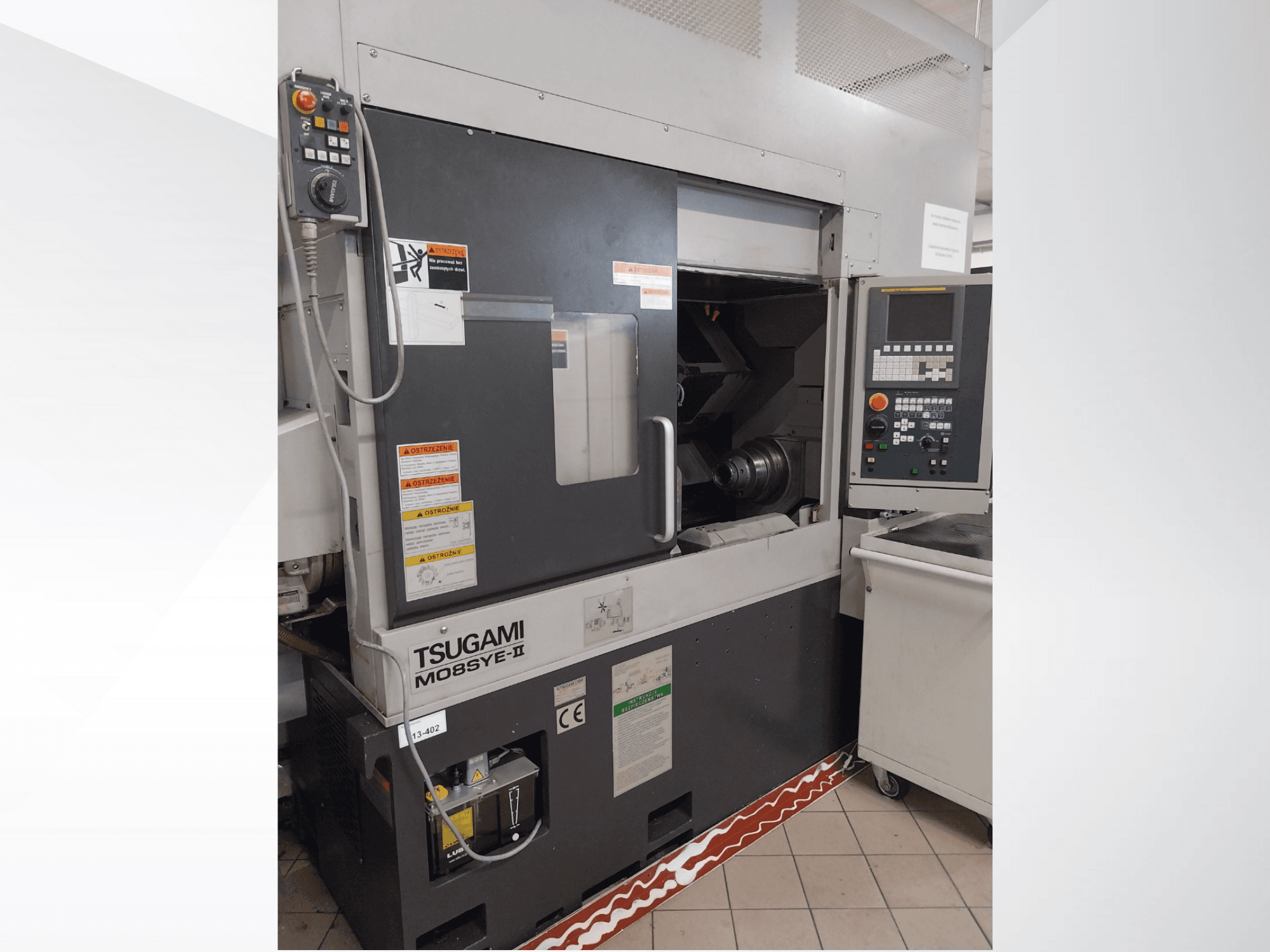 CNC soustruh Tsugami M08SY-II, pohled zepředu, zobrazující ovládací panel, vřeteno a ložnou plochu. Obsahuje bezpečnostní upozornění a štítek značky.