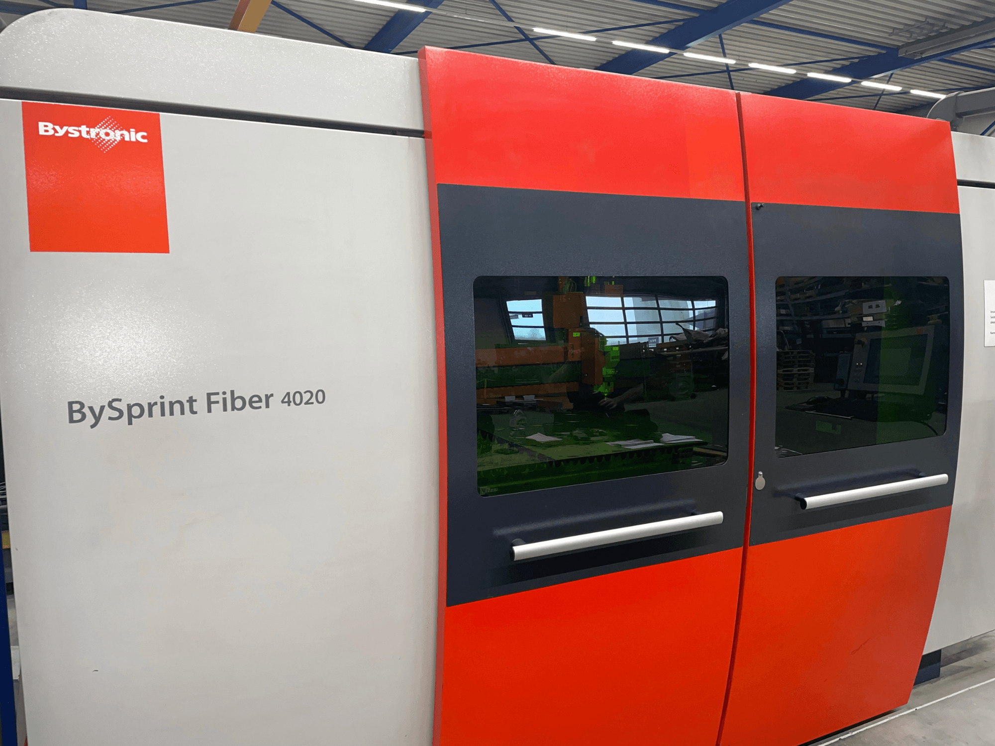 Bystronic BySprint Fiber 4020 v čelním pohledu, s šedočerveným designem panelu s velkými okny a ovládacím rozhraním viditelným uvnitř.