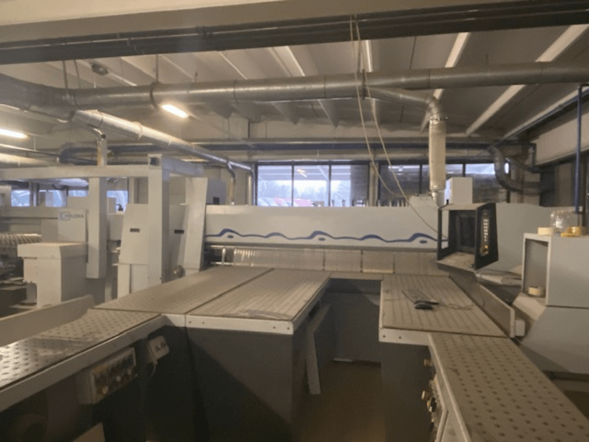 Průmyslové pracoviště se strojním zařízením a ovládacím panelem, pohled zepředu z vyvýšeného úhlu.