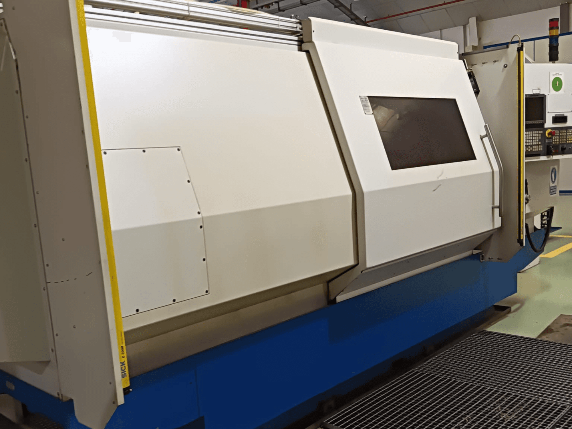 Průmyslový soustruh, pohled z boku, s velkým bílo-modrým krytem, digitálním ovládacím panelem a bezpečnostními prvky.