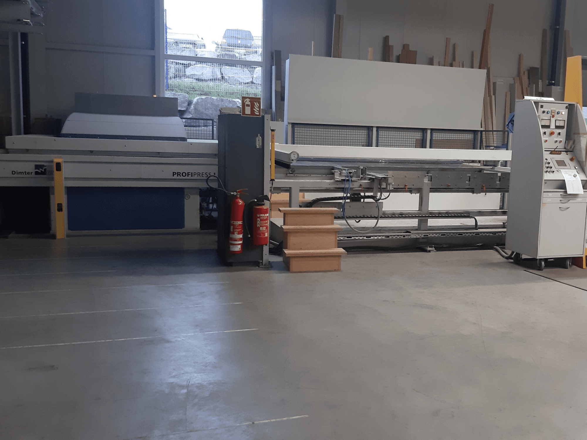 Stroj Dimter ProfiPress v dílně, pohled zepředu, s ovládacím panelem a hasicími přístroji v blízkosti.
