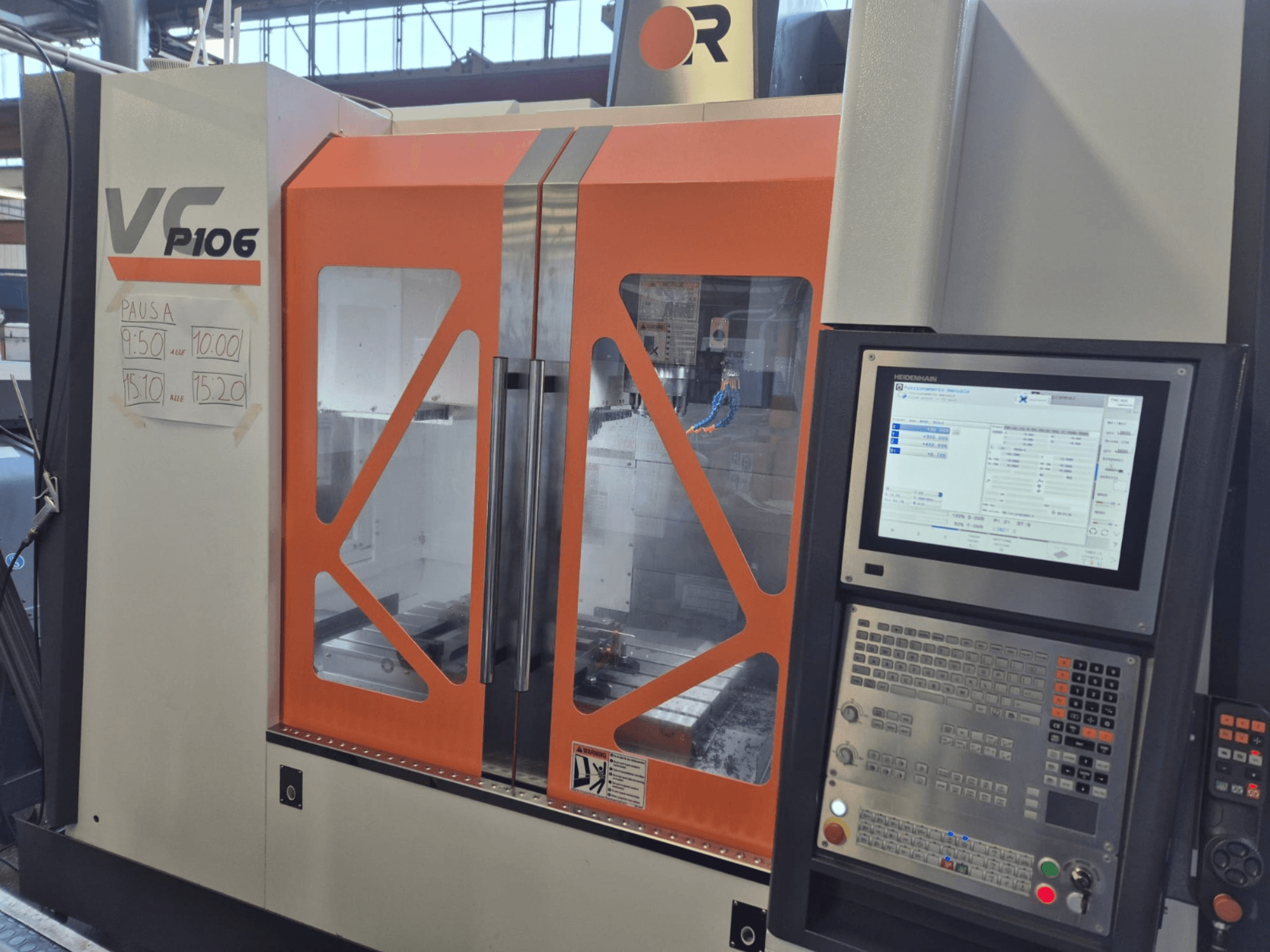 Alt text: Oranžovo-šedý stroj VF P106 CNC, pohled zepředu, zobrazení ovládacího panelu a plánovaných časů operací na papíře.