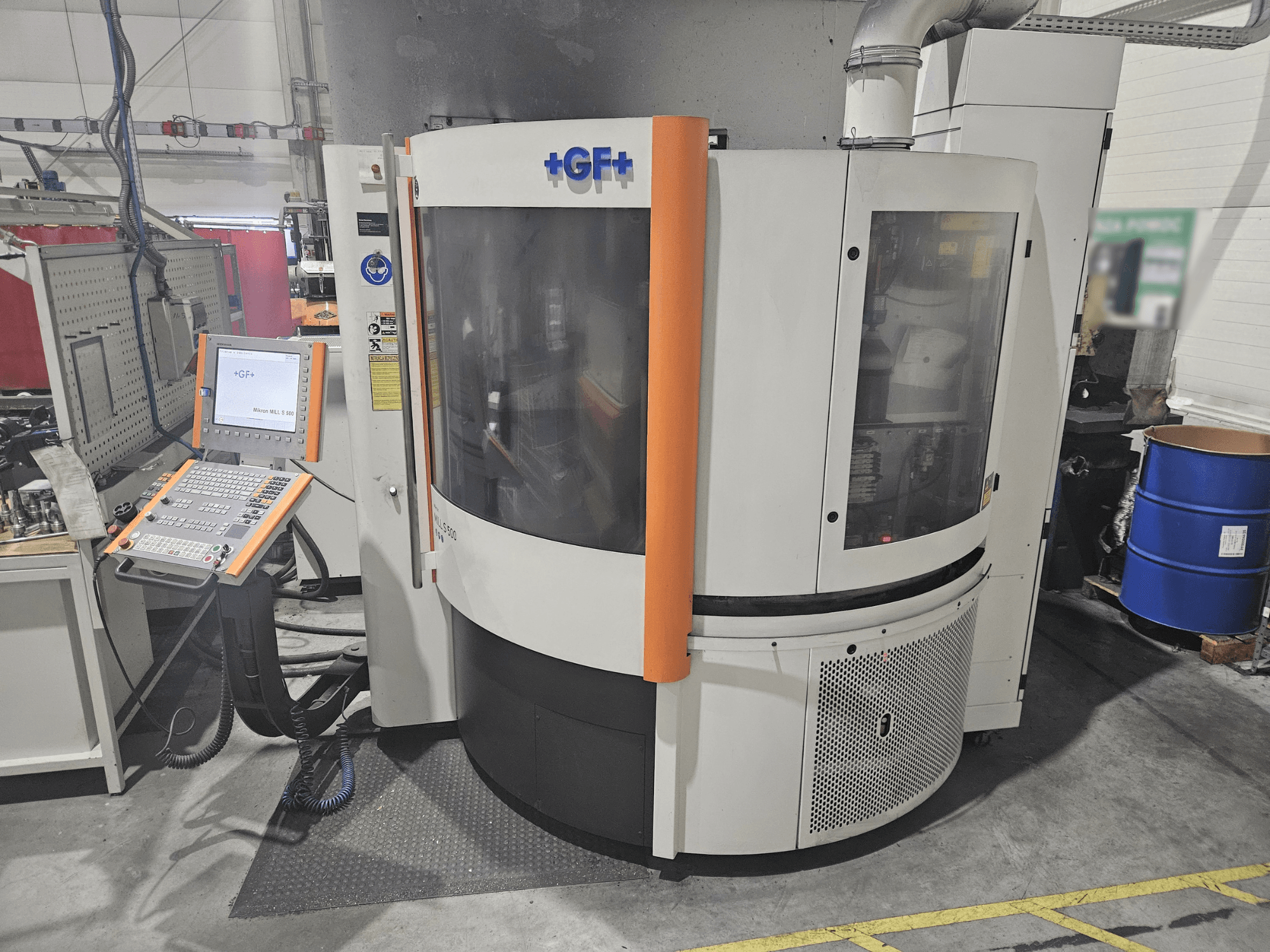 Obráběcí stroj GF Machining Solutions s ovládacím panelem, pohled zepředu; průhledný panel, oranžové akcenty a průmyslové nastavení.