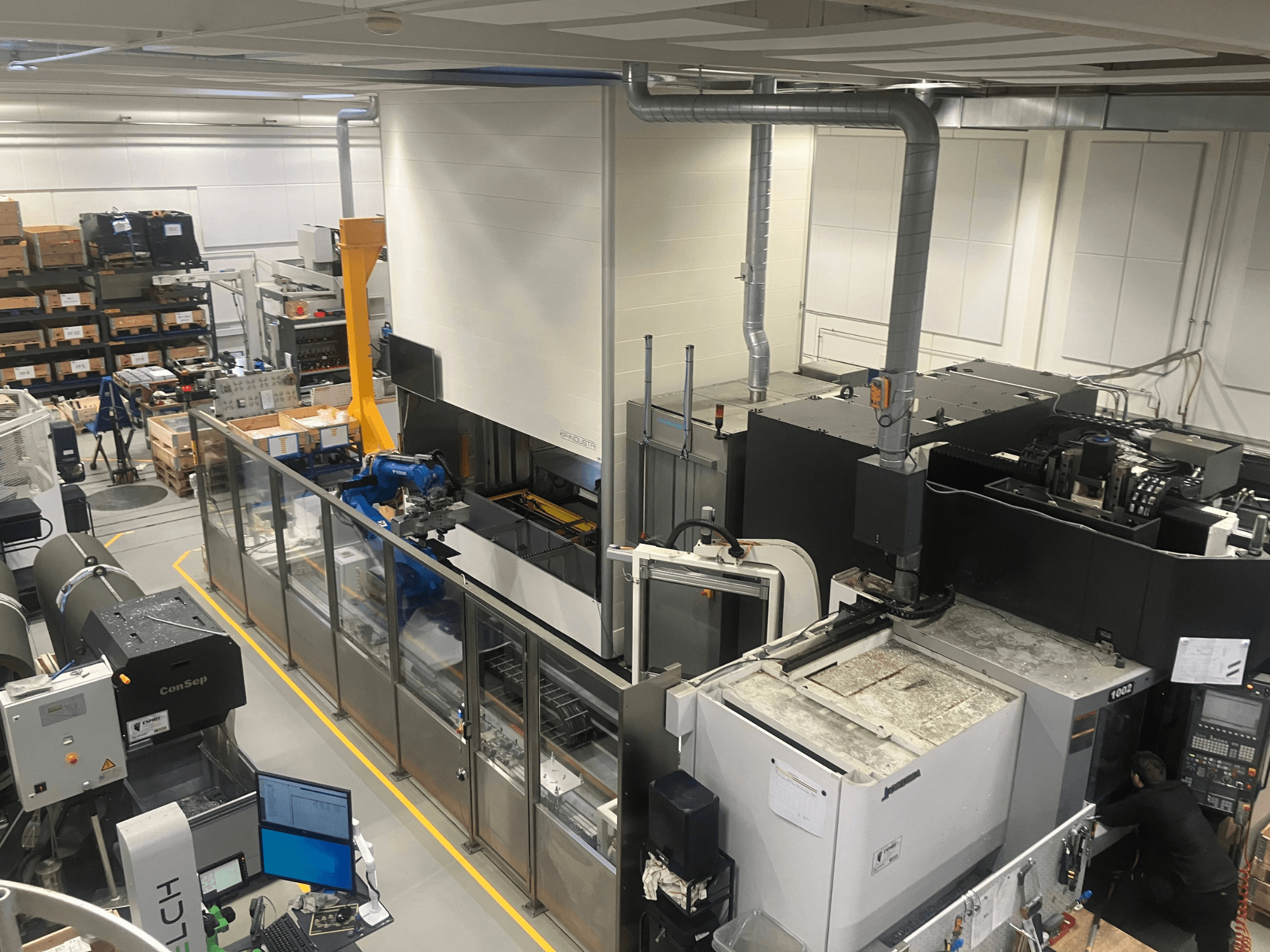 Automatizační systém SSI SCHAFER Logimat ve skladu, pohled zepředu; obsahuje robotické rameno, skladovací regály a stroje.