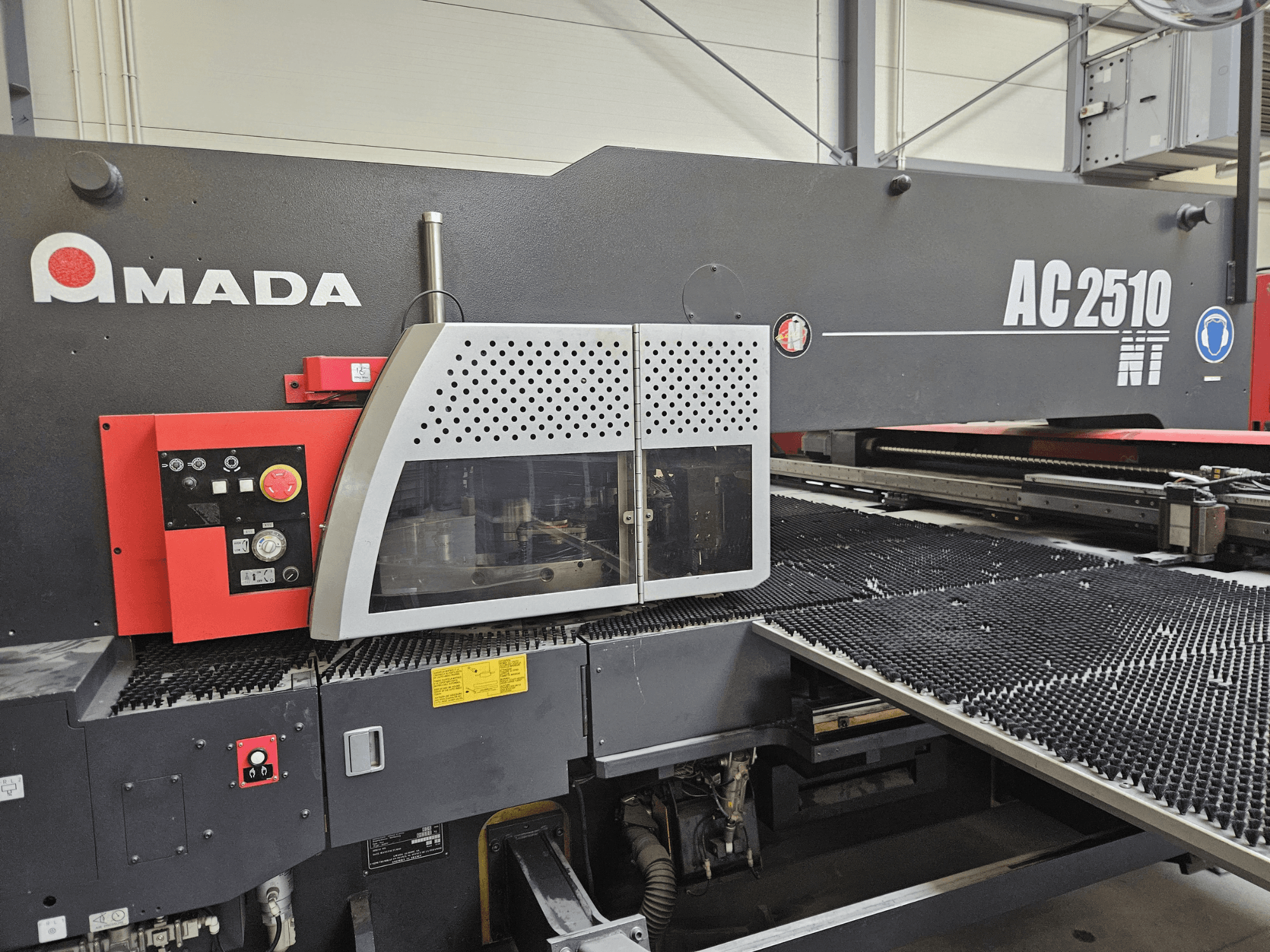 Laserový řezací stroj Amada AC2510 NT, pohled zepředu, ovládací panel s knoflíky, tlačítky a bezpečnostním krytem.