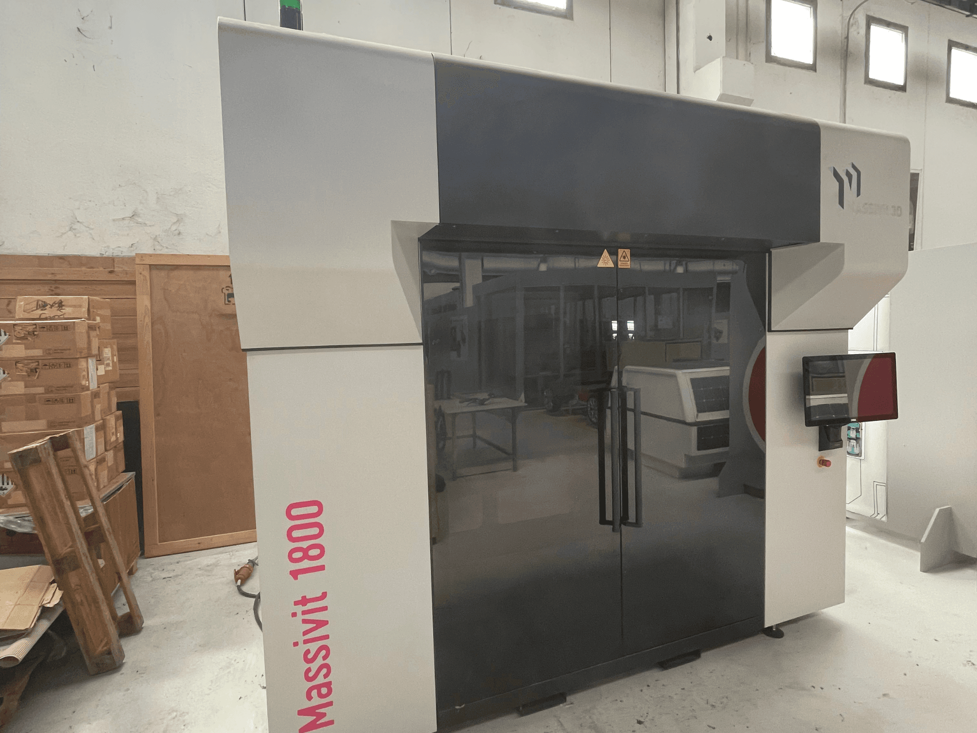 Plastová 3D tiskárna MASSIVIT Massivit 1800 zobrazená z boku, vybavená dotykovým displejem a elegantním černobílým designem.