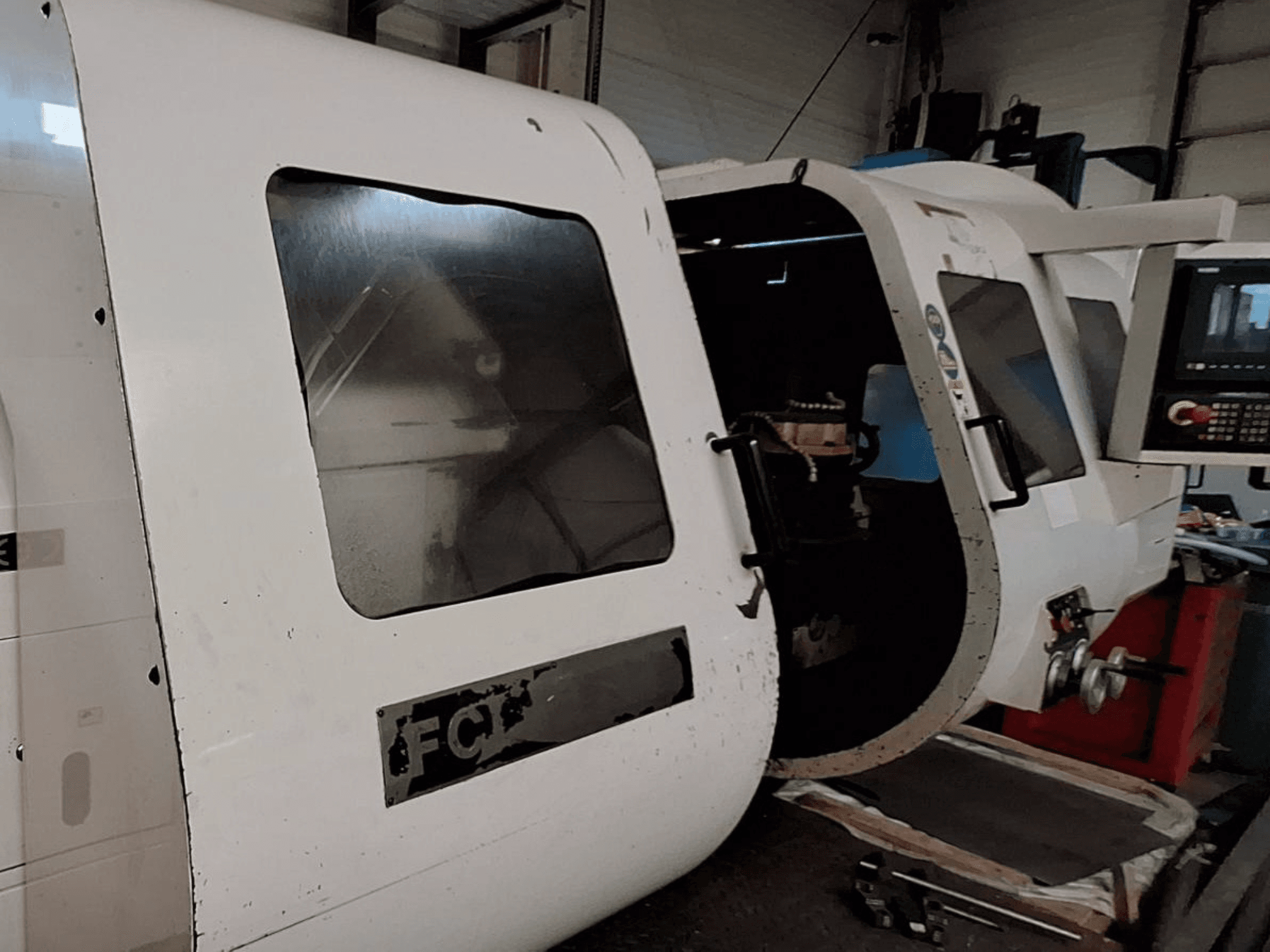 Bílý CNC stroj s viditelným ovládacím panelem a otevřenými dveřmi, které ukazují vnitřní komponenty; pohled zepředu. Značka: FCT.