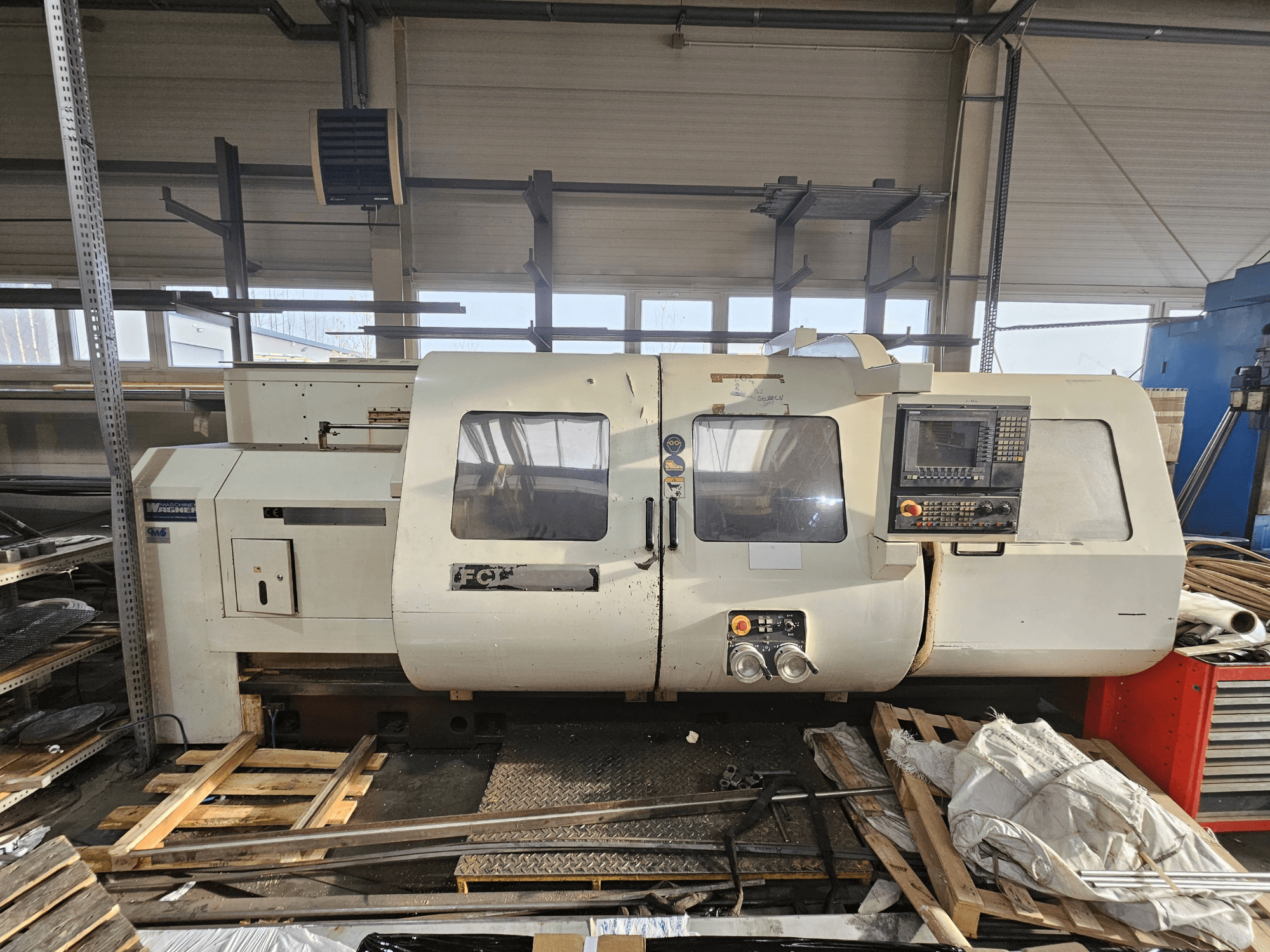 CNC soustruh Wabeco, boční pohled, ovládací panel, okna a pracovní plocha; stroje na dřevěných paletách v dílně.