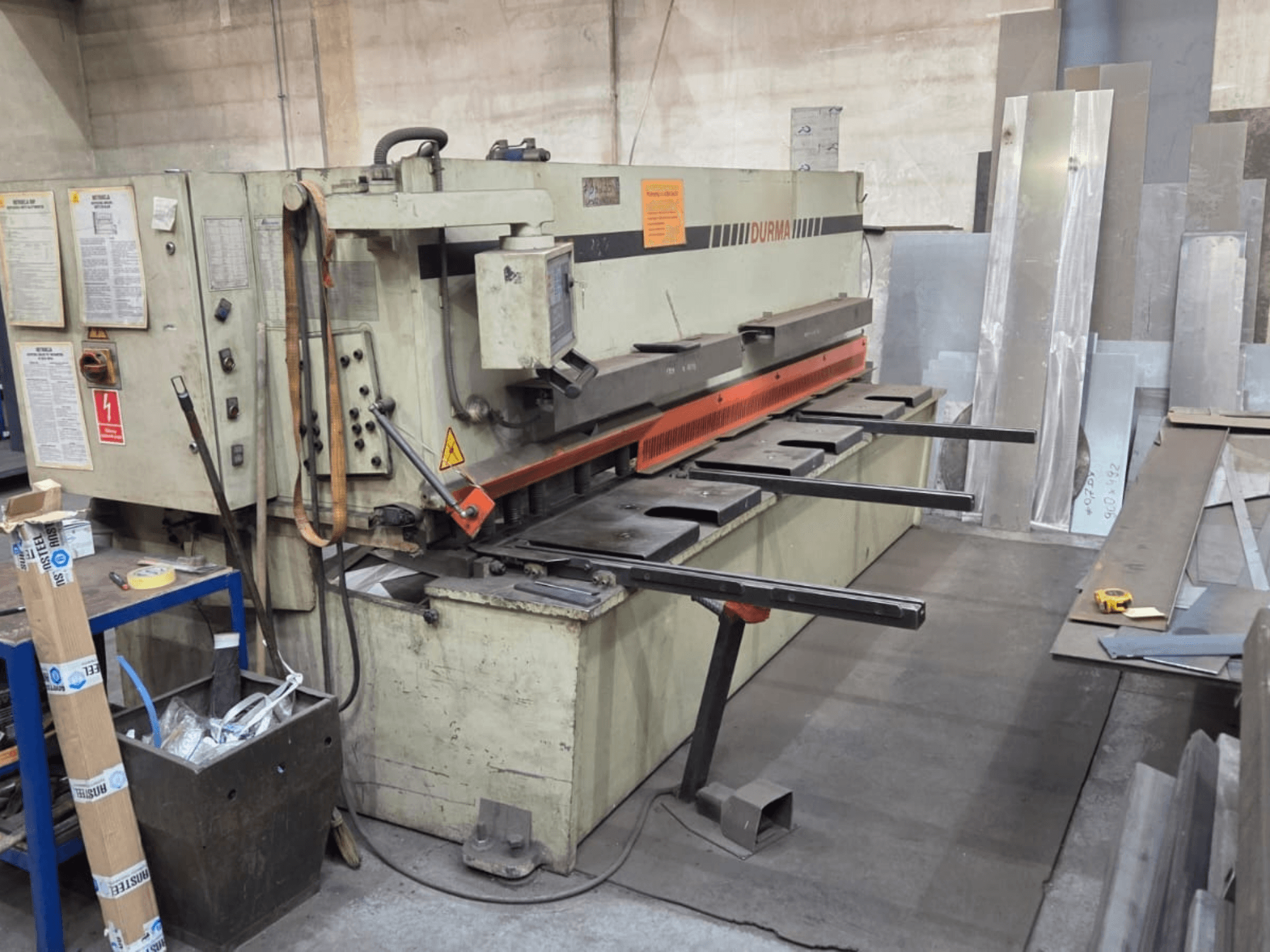 Hydraulické nůžky Durma SB 3060, pohled zepředu, zobrazující ovládací prvky, řezací nůž a plechy v pracovním prostoru.