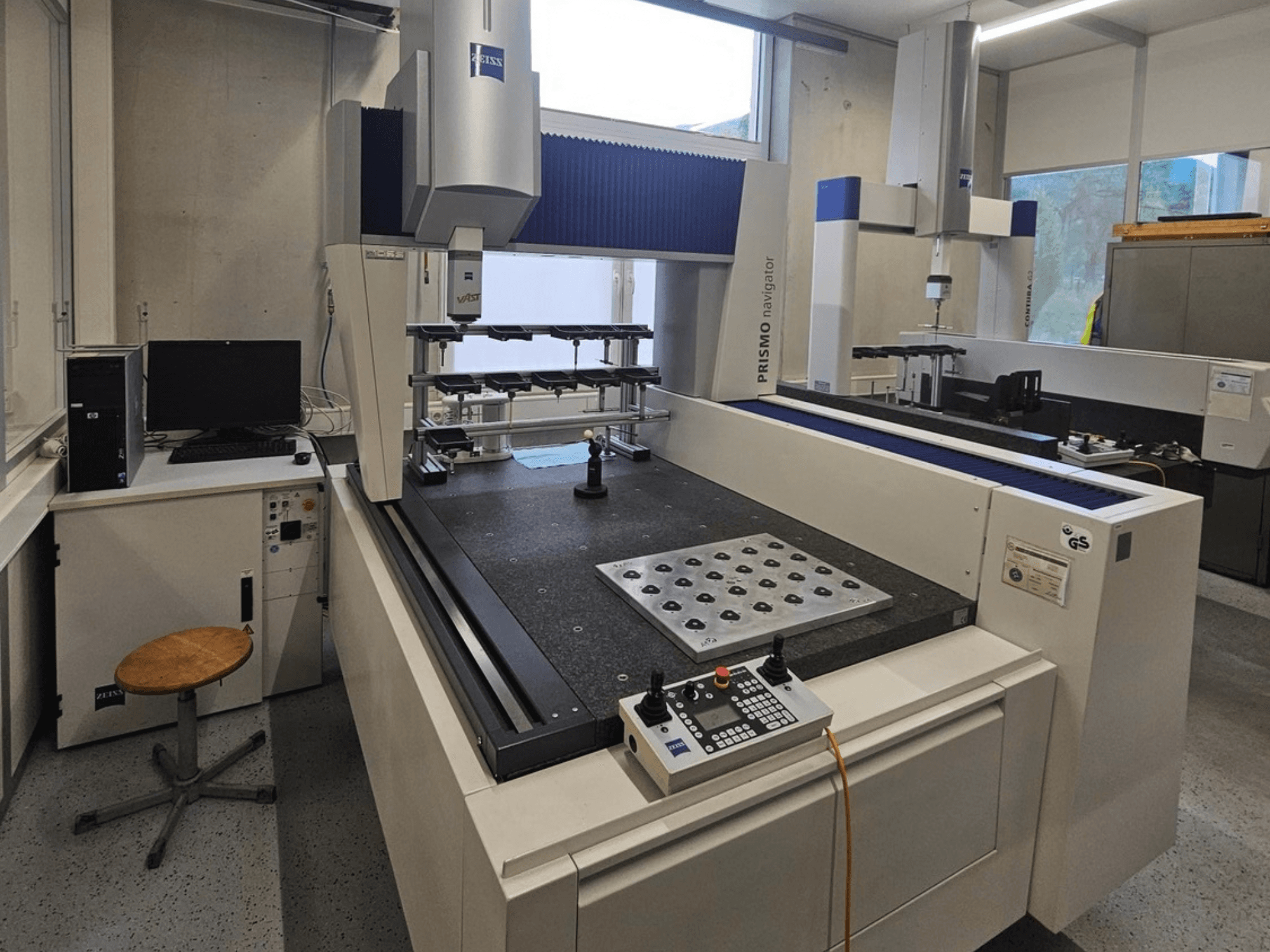 Koordinátový měřicí stroj ZEISS Prismo Navigator 7 v laboratoři, pohled zepředu na ovládací panel, pracovní stůl a monitor.
