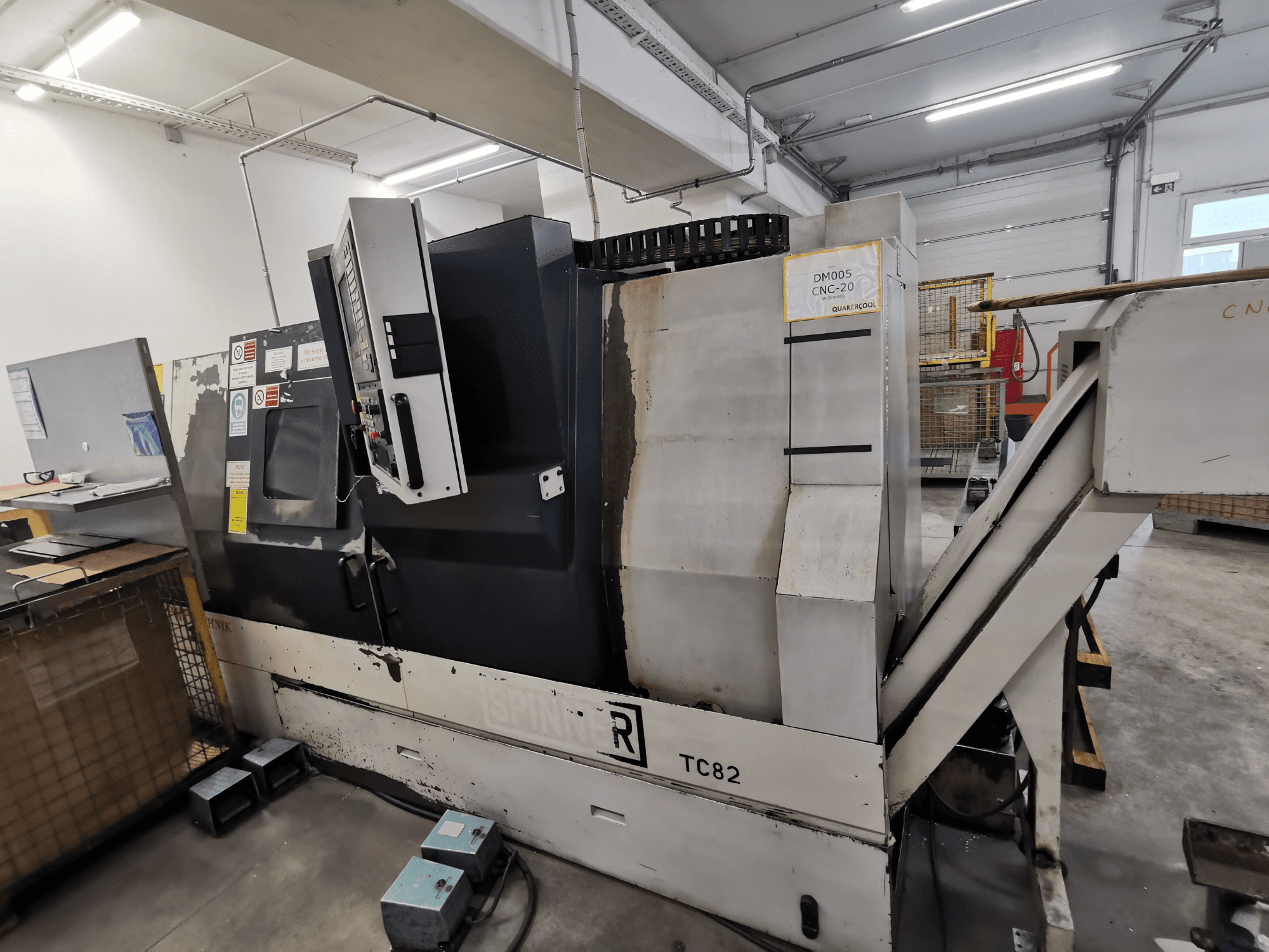 CNC stroj značky Spinner, model TC82, boční pohled zobrazující ovládací panel a žlab pro odstraňování šrotu v dílně.