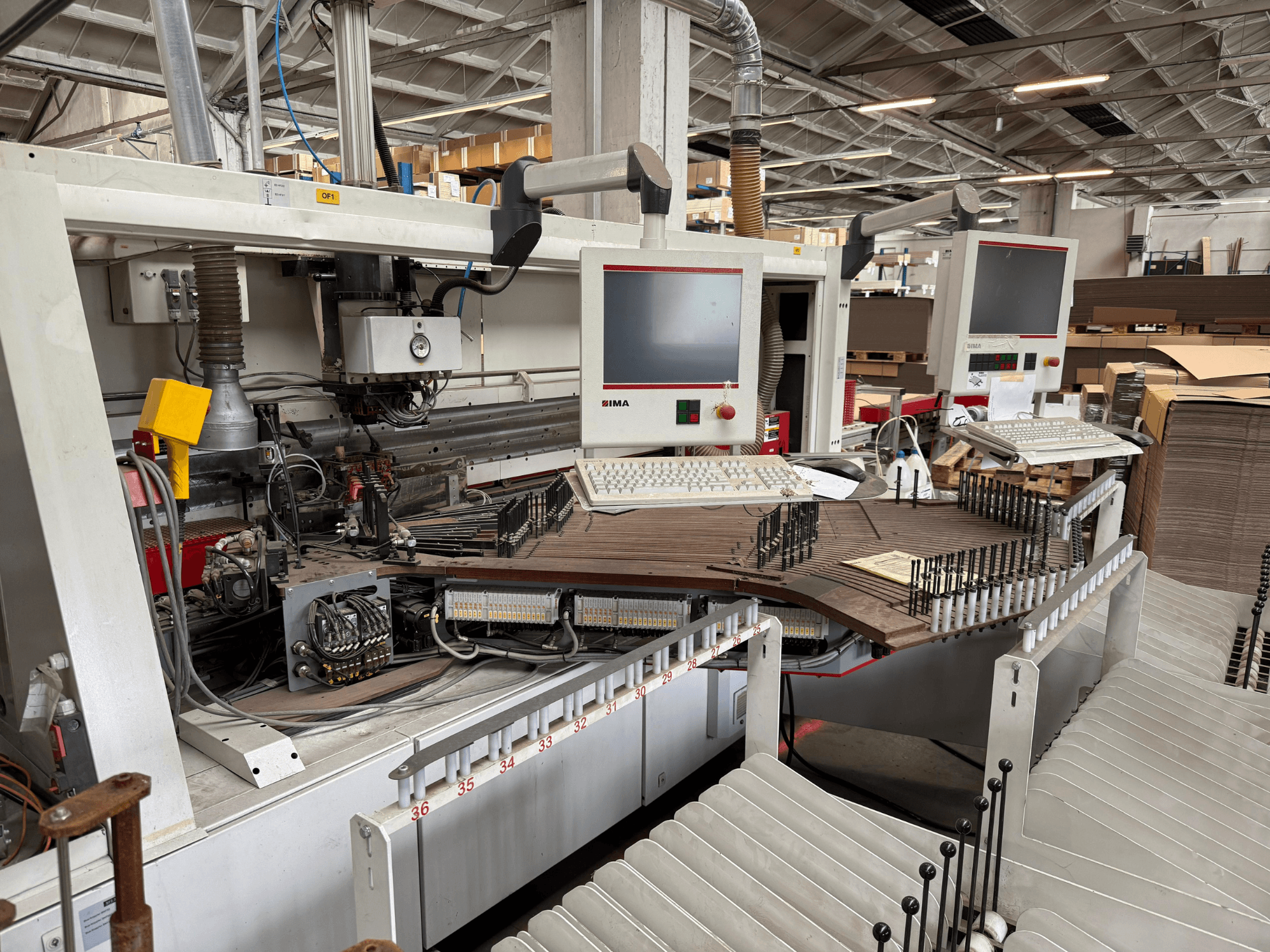 Přesný dřevoobráběcí stroj IMA se dvěma monitory a ovládacími panely, pohled zepředu ukazuje dopravník a prostor pro nástroje.