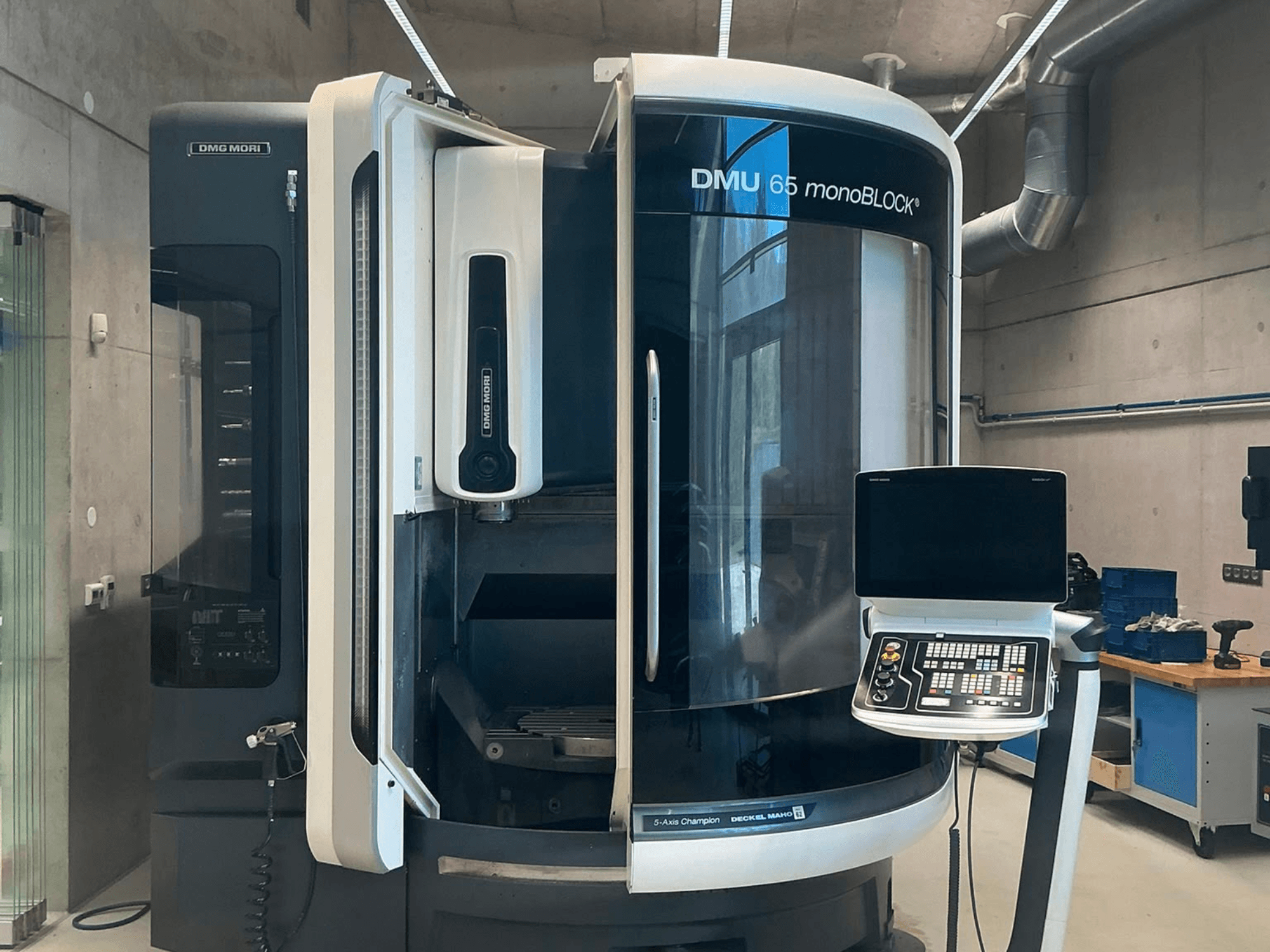 Vertikální obráběcí centrum DMG MORI DMU 65 monoBLOCK, pohled zepředu, znázorňující ovládací panel a detaily stroje v dílenském prostředí.