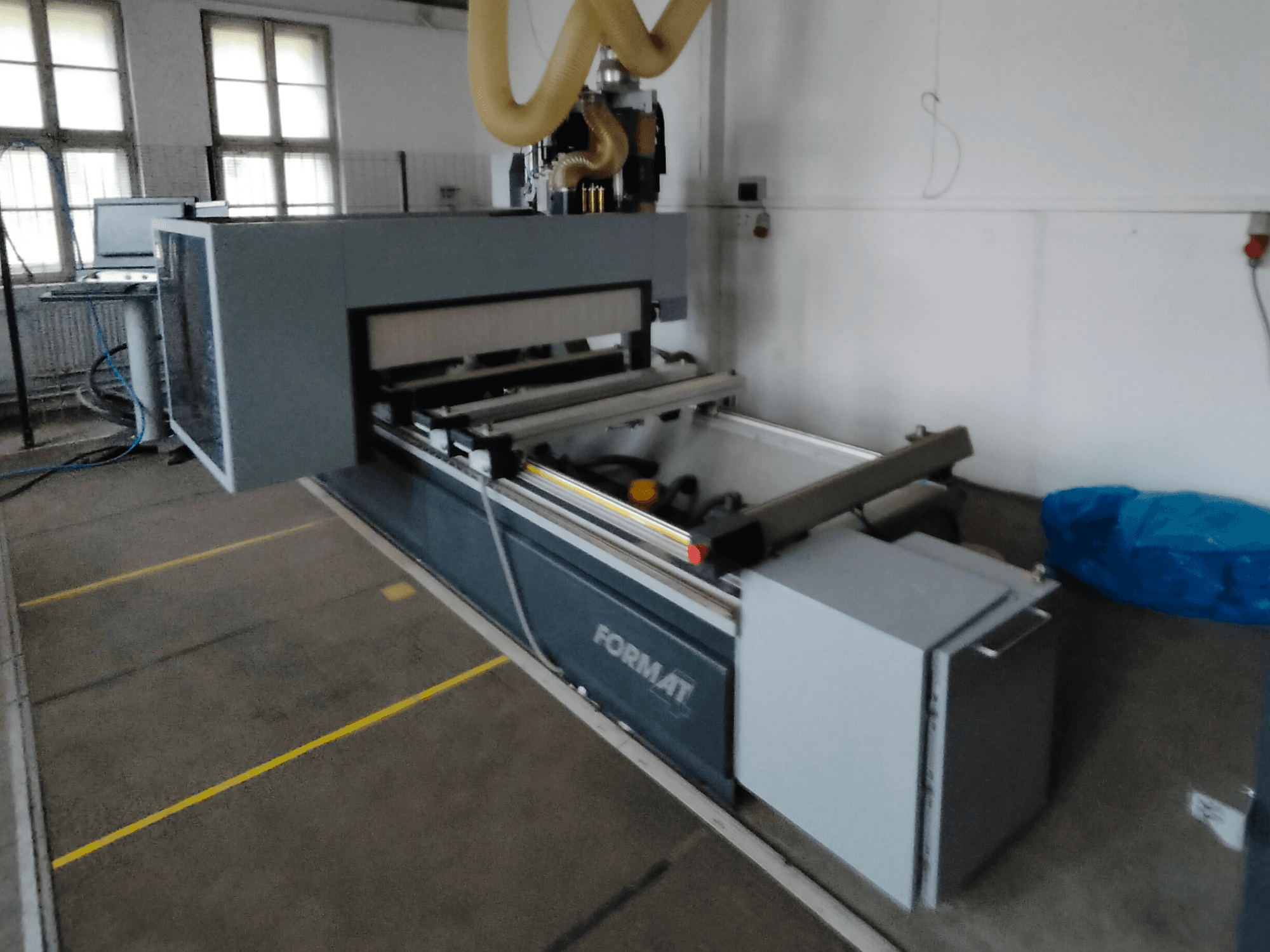 Pohled zepředu na stroj Format CNC s šedým tělem, vodicími lištami a viditelným ovládacím panelem.