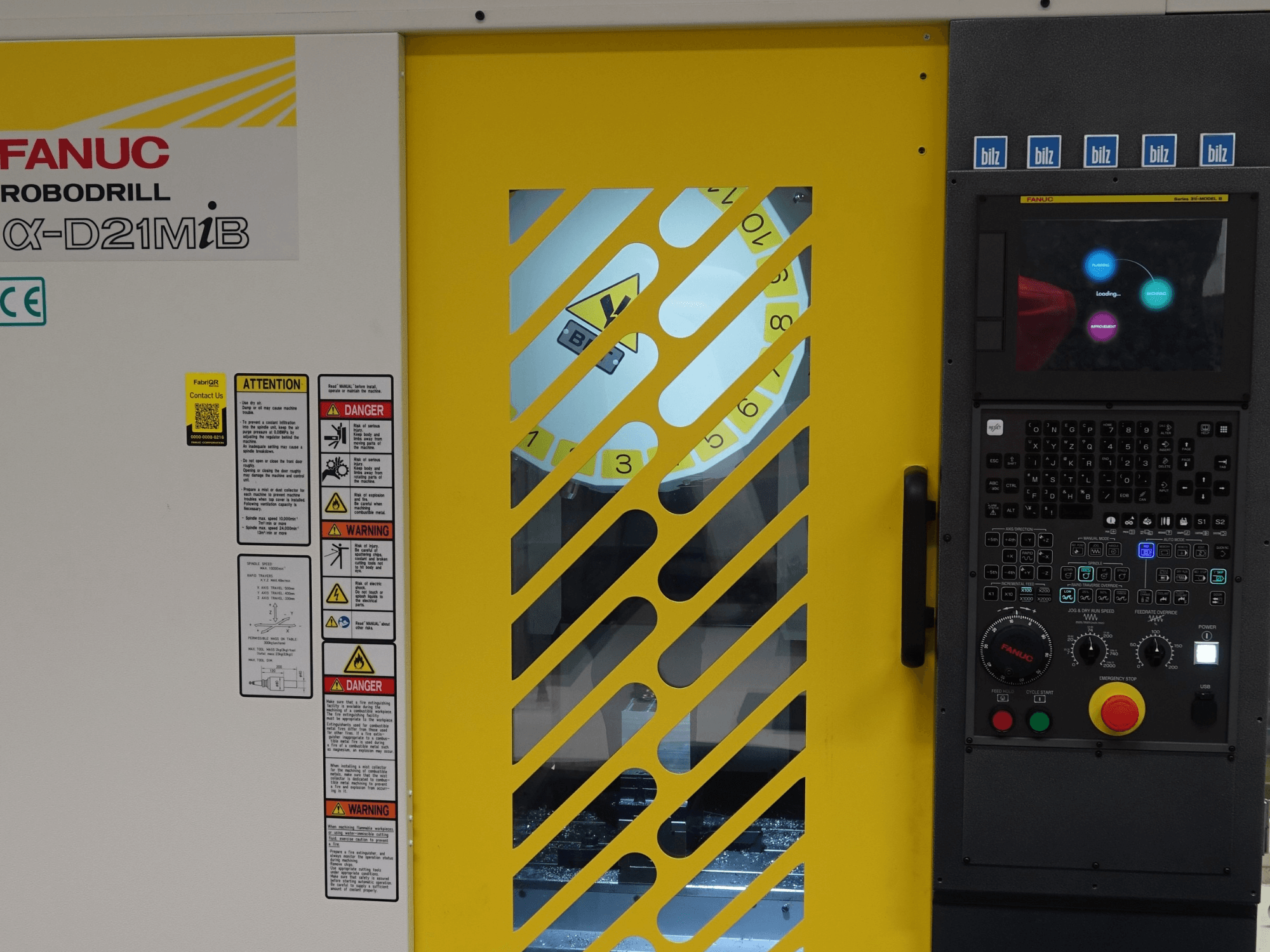 Vertikální obráběcí centrum FANUC α-D21MiB – pohled zepředu, na kterém jsou vidět bezpečnostní varování, ovládací panel a žluté bezpečnostní dveře.
