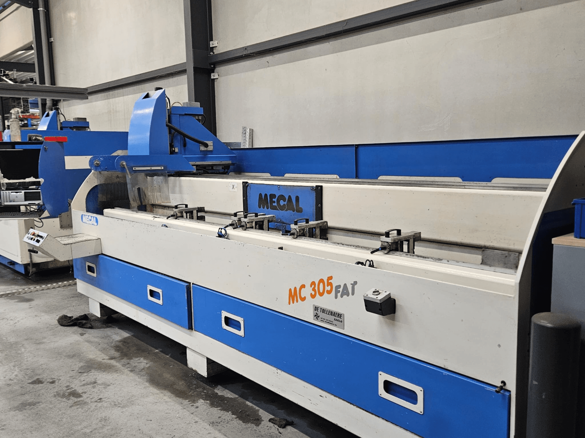 Stroj MECAL MC 305 FAT v továrním prostředí, čelní pohled na ovládací prvky a modrobílý design.