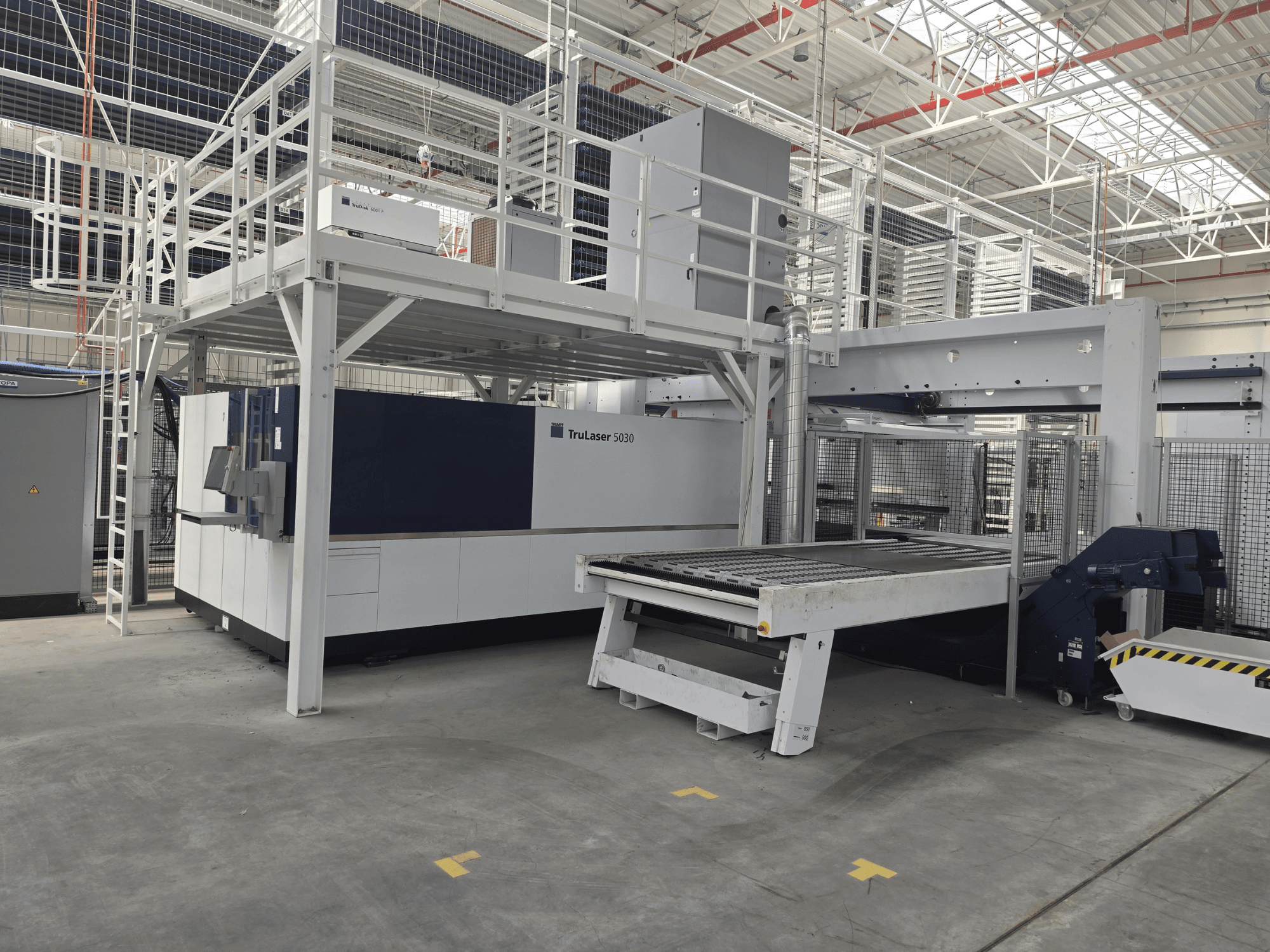Stroj TRUMPF TruLaser 5030 fiber L76 FMC v dílně, pohled zepředu znázorňující řezací plochu a mechanismus nakládání a vykládání.