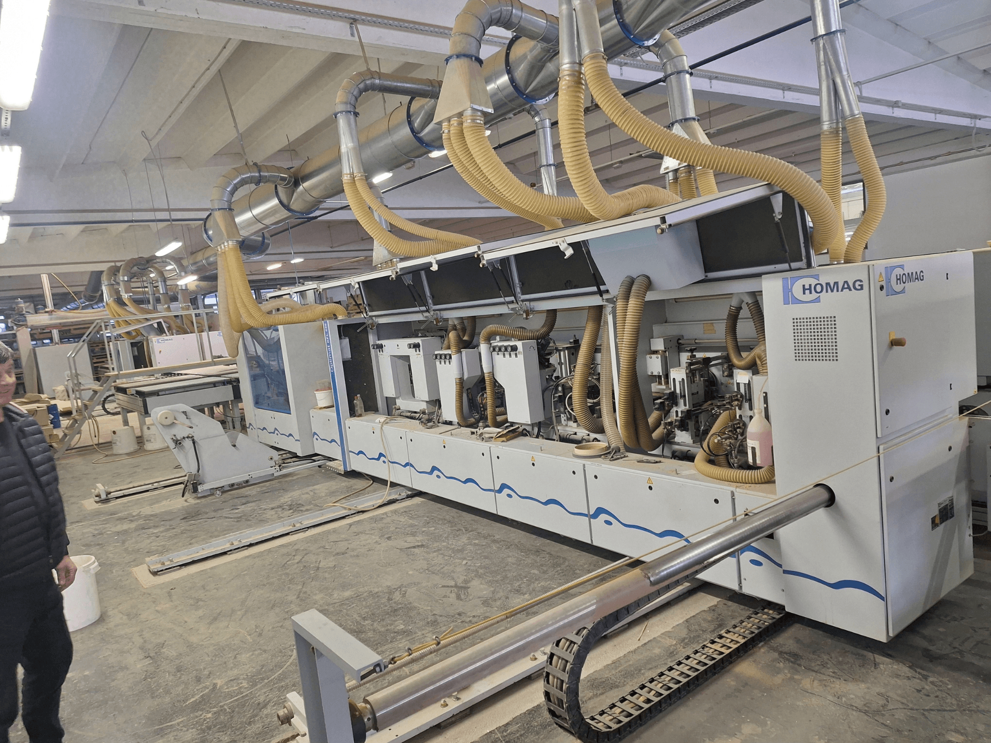 Dřevoobráběcí stroj HOMAG v továrním prostředí, pohled zepředu ukazuje několik vřeten a systém odsávání prachu.