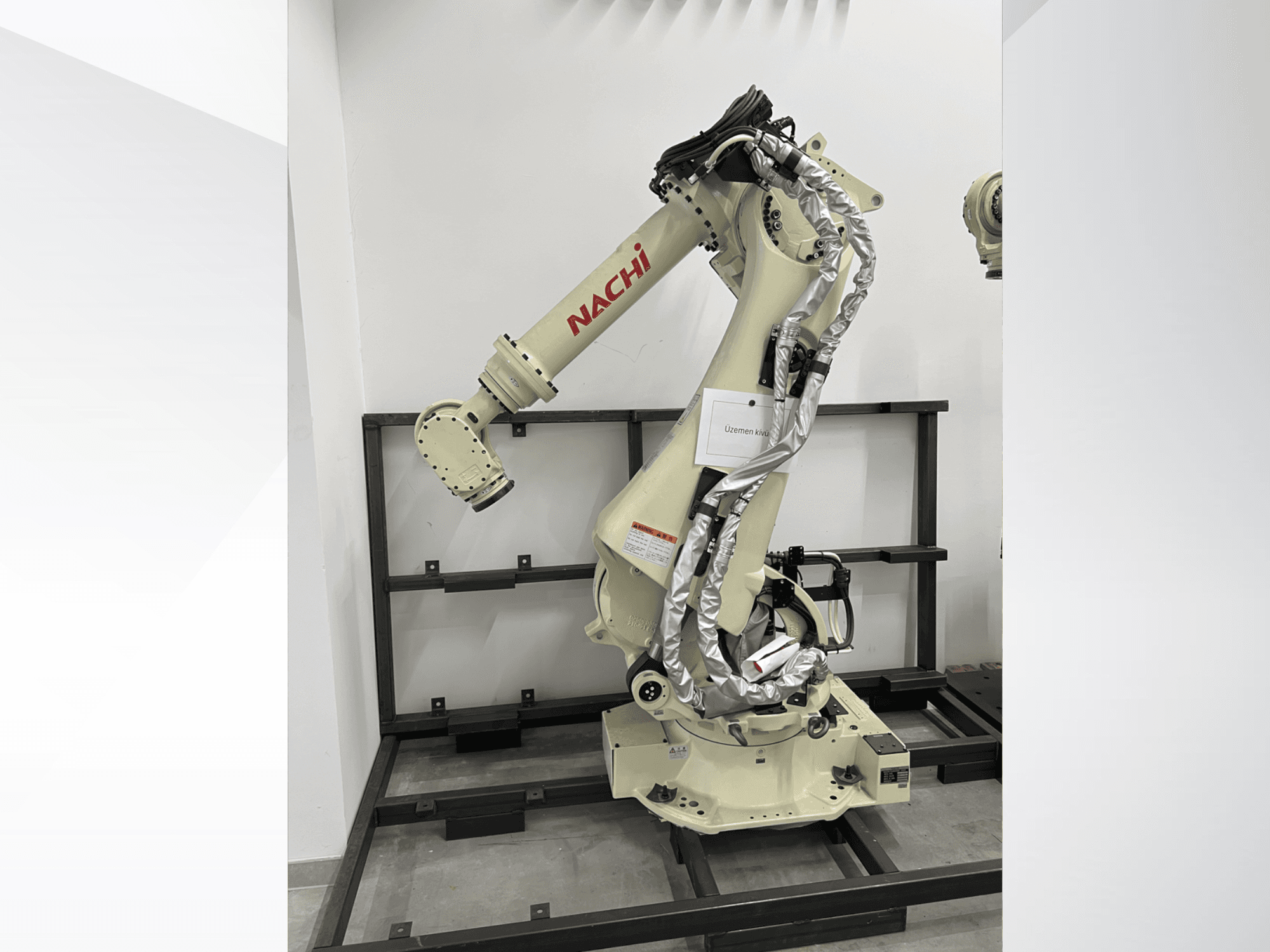 Robotické rameno NACHI SRA166-01 v bočním pohledu, s ohebnými klouby, připojenými kabely a namontované na ochranném rámu.