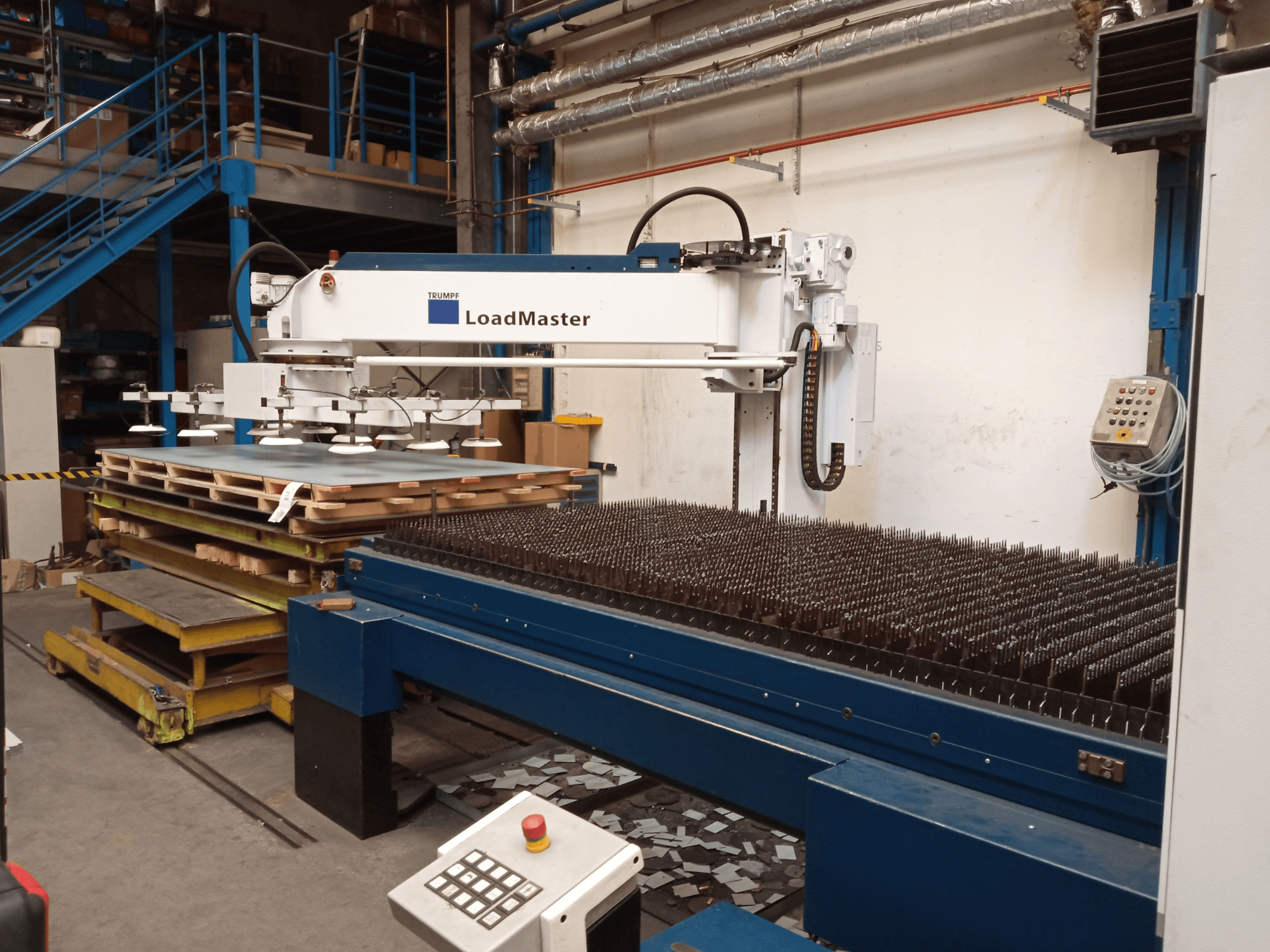 CO₂ laserový řezací stroj TRUMPF TruLaser 3030 v bočním pohledu, vybavený zařízením LoadMaster a paletami s materiálem.