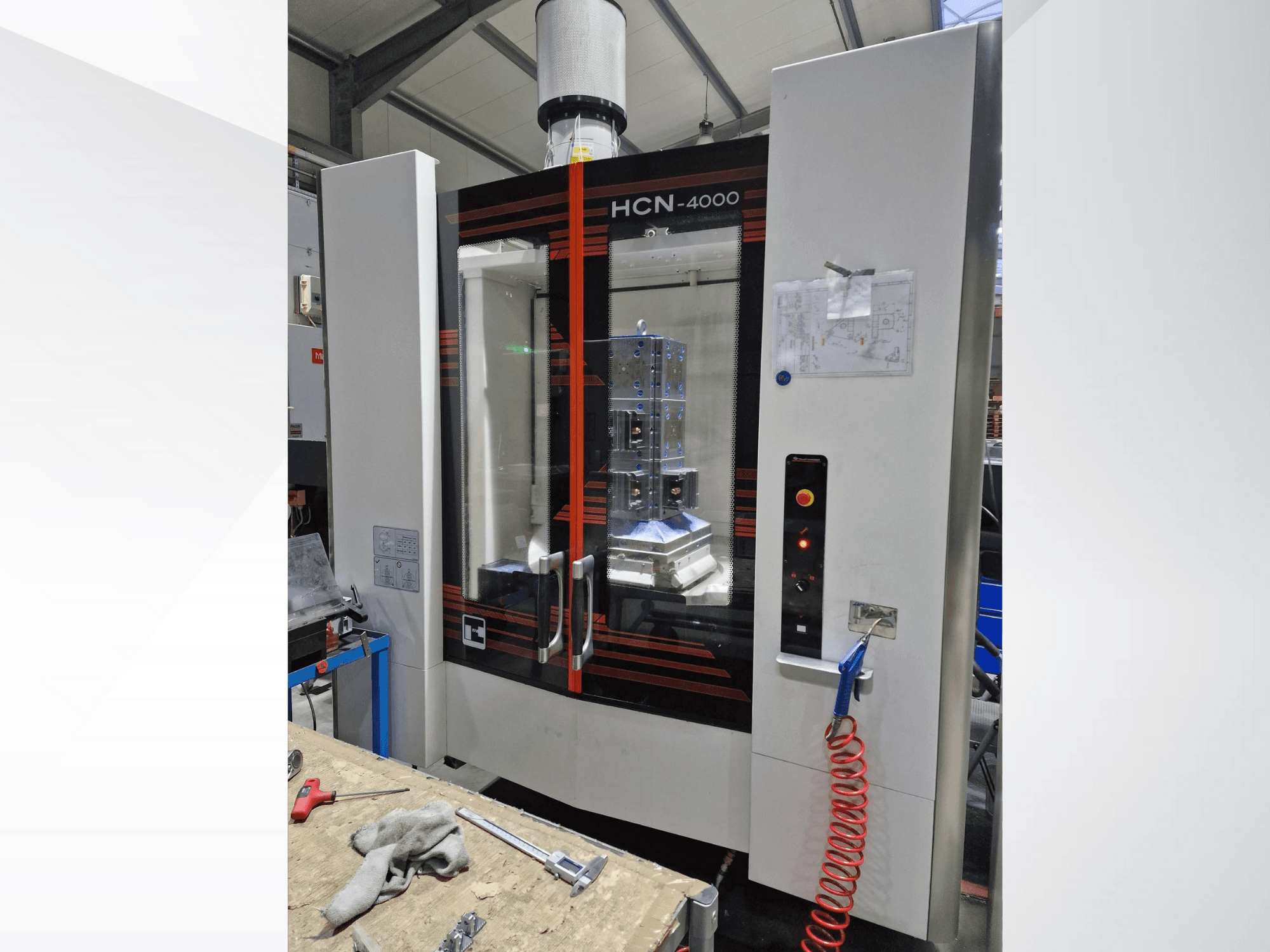 Stroj HCN-4000 CNC v čelním pohledu, se skleněným panelem, ovládacím panelem s tlačítky a přiloženým plánem.