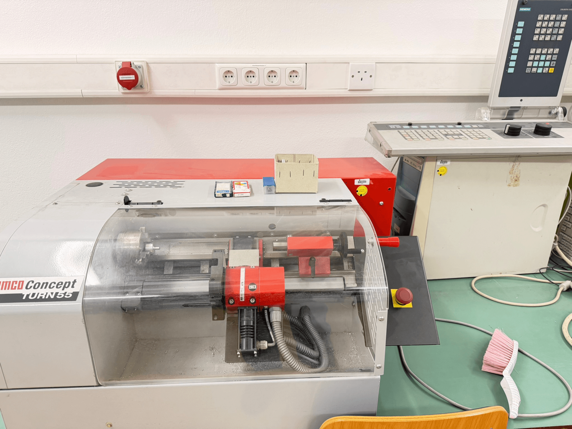 Horizontální soustruh EMCO Concept Turn 55 s červeným a šedým exteriérem, pohled zepředu ukazuje ovládací prvky a pracovní prostor.