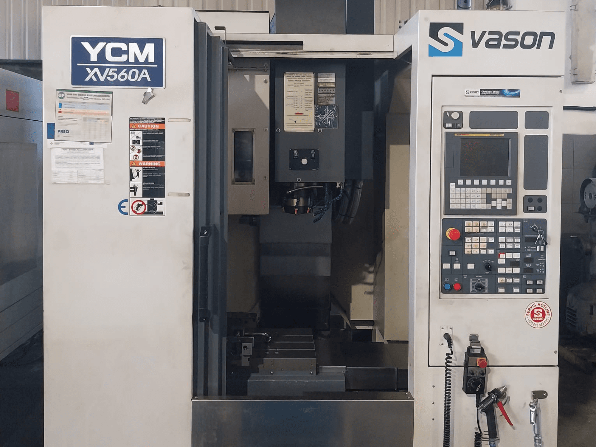 Pohled zepředu na vertikální obráběcí centrum YCM XV 560A, s viditelným ovládacím panelem a pracovním stolem s obráběcími komponenty.