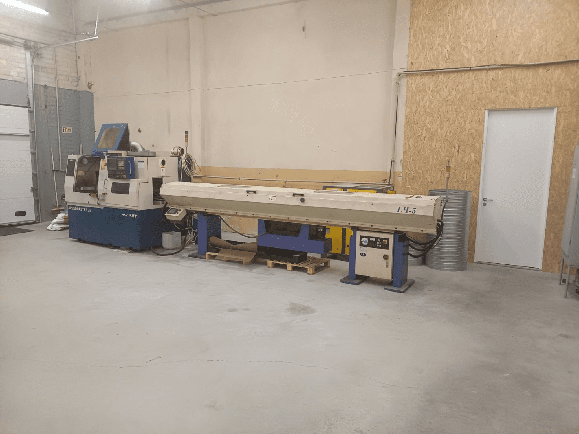 Průmyslová dílna se stroji KMT Speedmaster 34 a L4.5, pohled zepředu, s viditelnými ovládacími prvky a strojním zařízením.