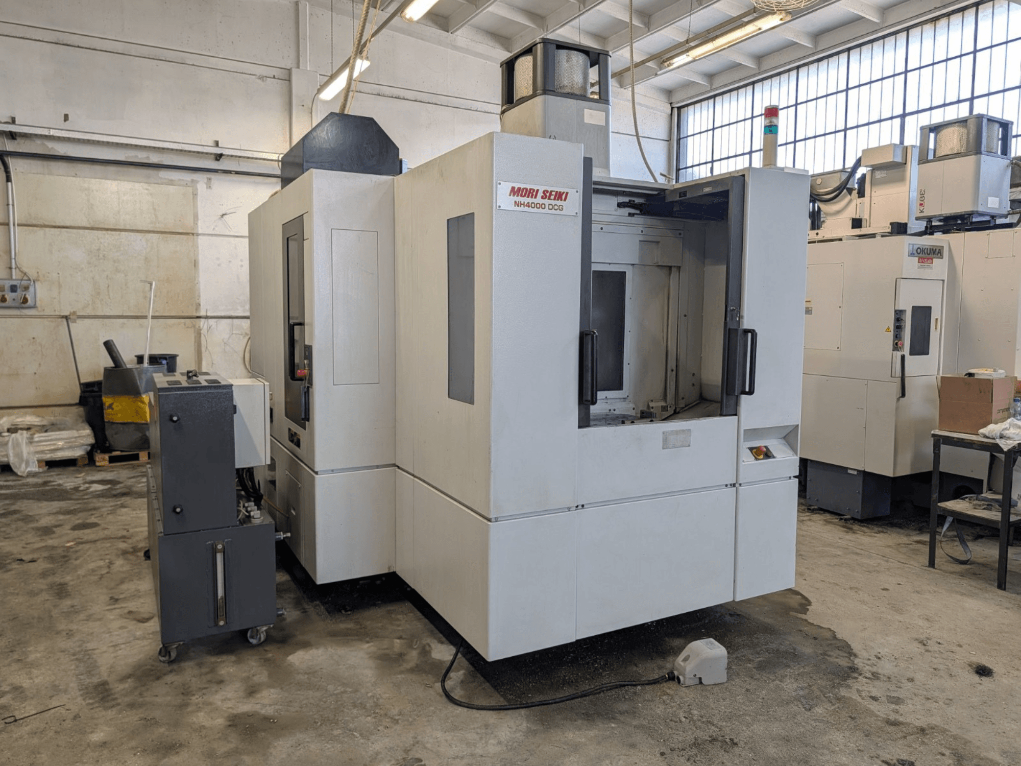 Horizontální obráběcí centrum MORI SEIKI NH 4000 DCG, pohled zepředu, ovládací panel a pracovní plocha, šedobílé provedení.