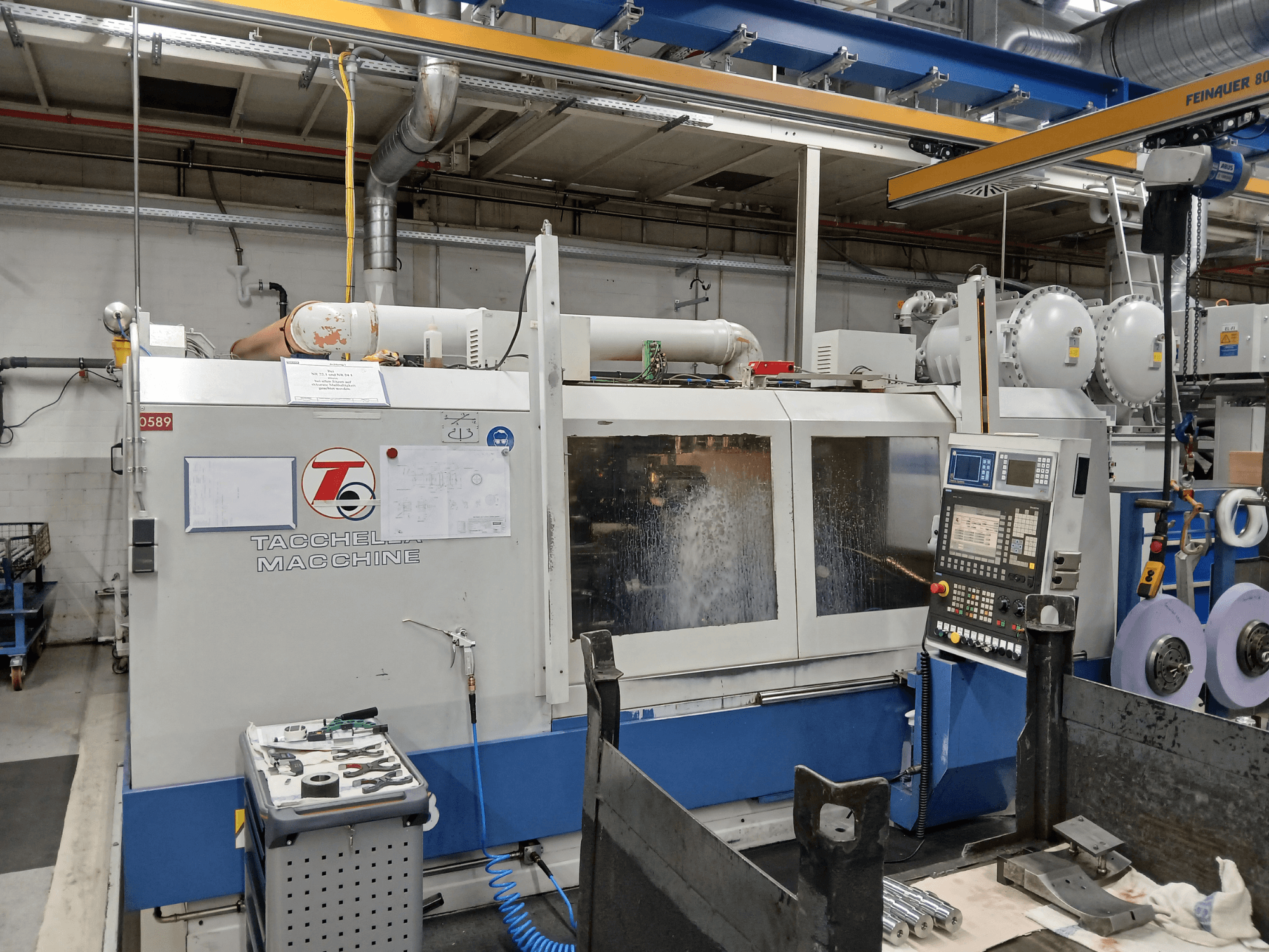 Obráběcí centrum Tacchella z čelního pohledu, s viditelným ovládacím panelem a nástroji. Vodní chladicí kapalina stříká během provozu.