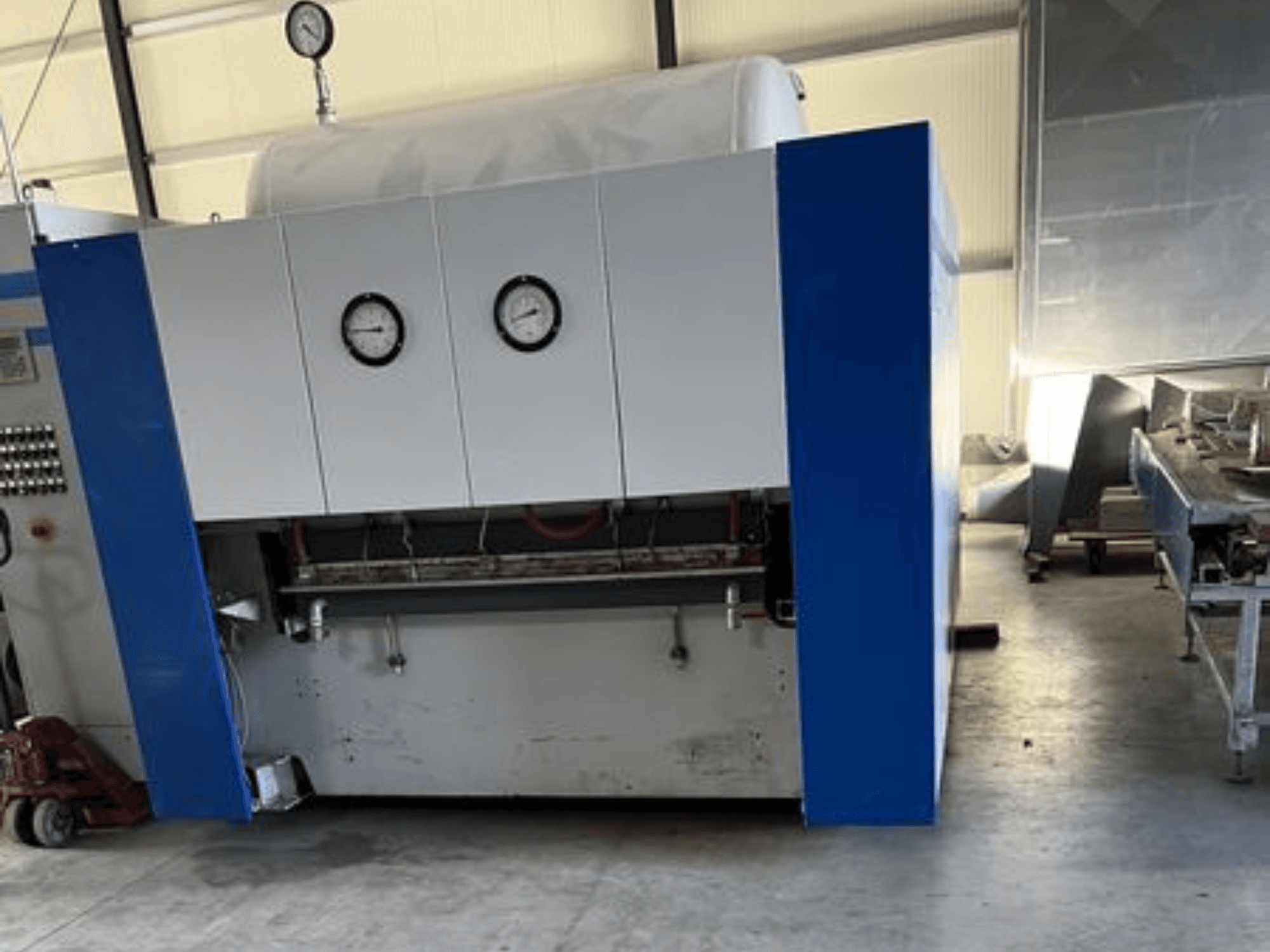 Modrobílý průmyslový stroj se dvěma tlakoměry, pohled zepředu, s ovládacím panelem a přilehlým zařízením.