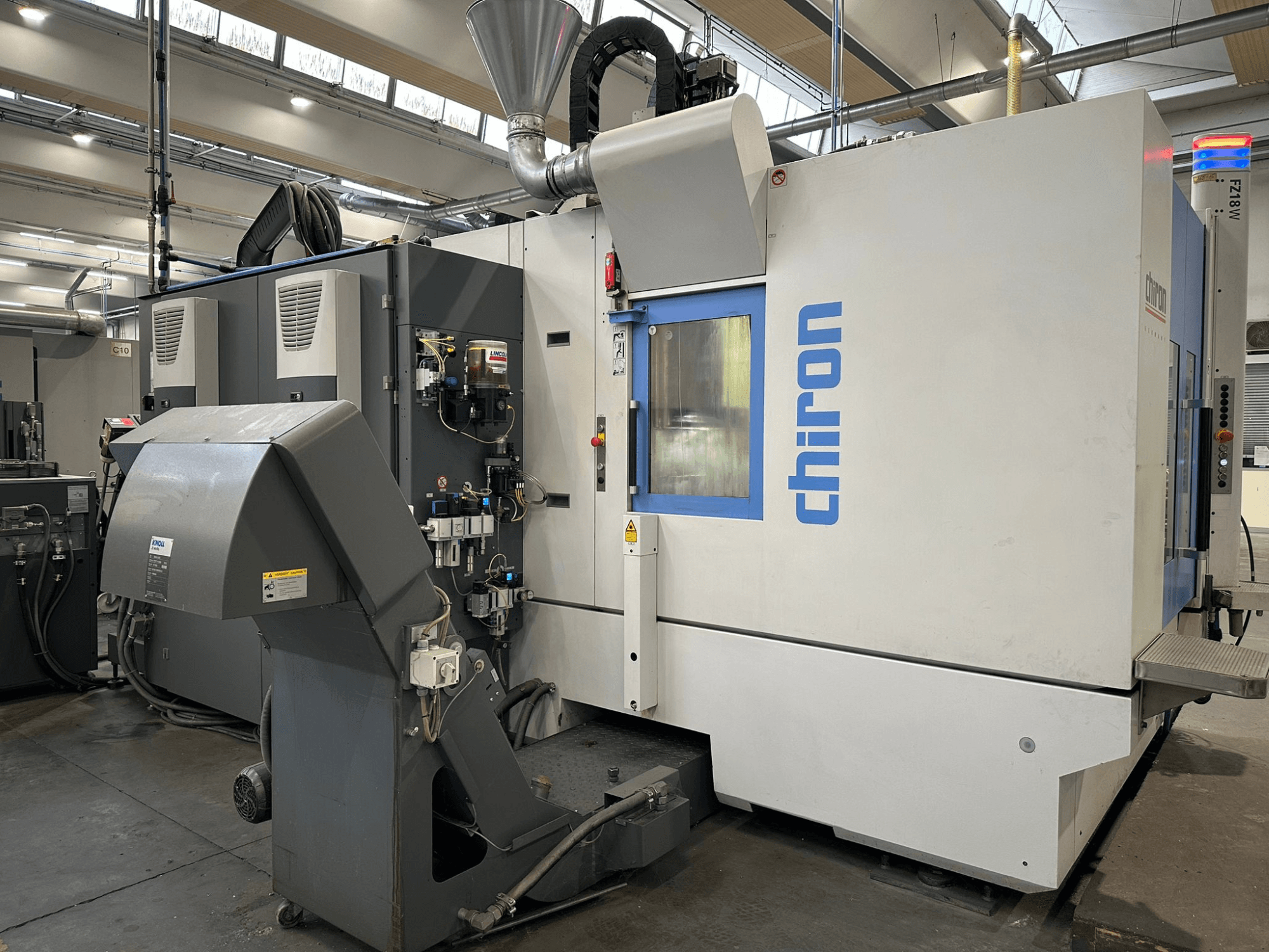 Stroj Chiron CNC v šedobílé barvě, pohled zepředu, s ovládacími prvky, trubkami a krytem pro odsávání prachu.