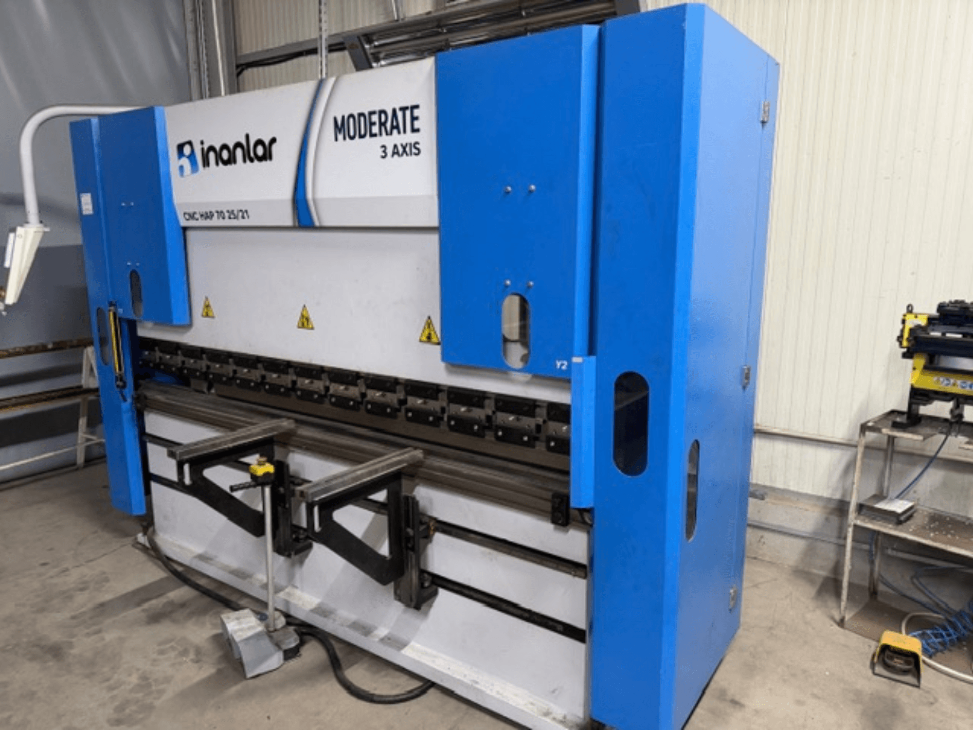 Inanlar Moderate 3osý CNC stroj v modré barvě, pohled zepředu, ovládací páky a bezpečnostní štítky viditelné na tělese.