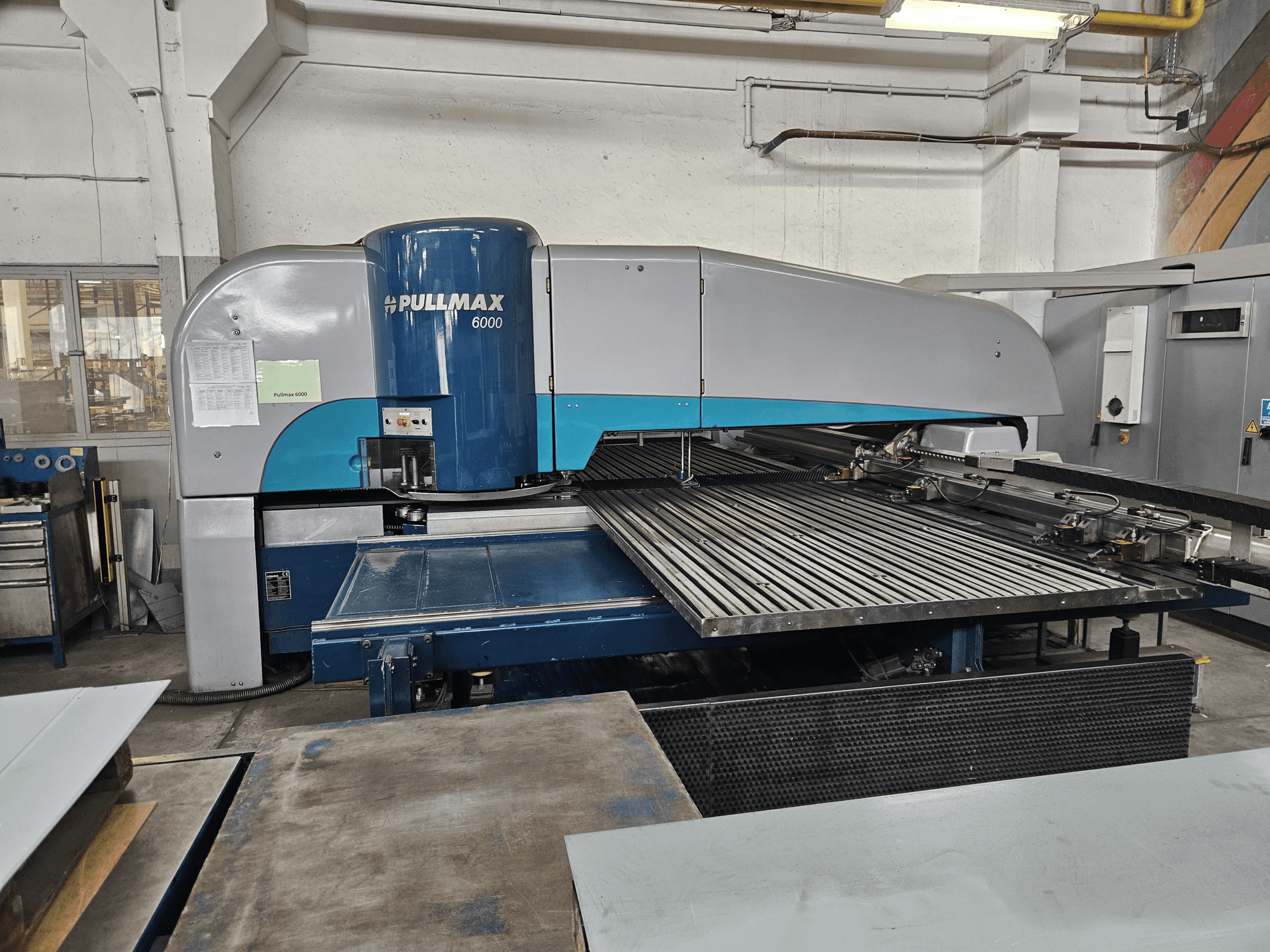 Pohled zepředu na CNC děrovací stroj Pullmax 6000, na kterém je vidět jeho velká plochá deska a kovový rám v dílenském prostředí.