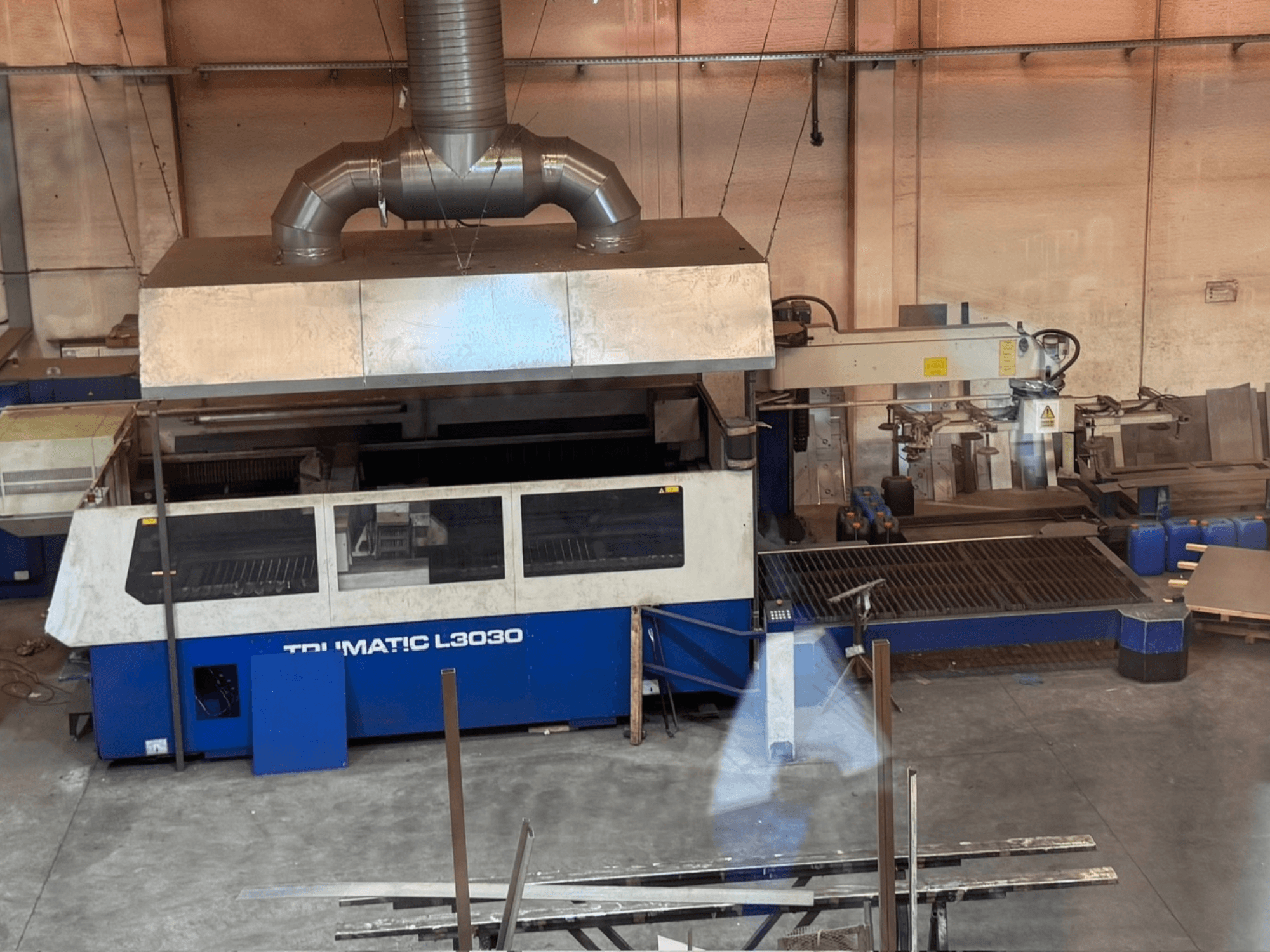 Stroj na řezání CO₂ laserem TRUMPF TRUMATIC L3030 v dílně, pohled zepředu s ovládacím panelem a řezacím stolem.
