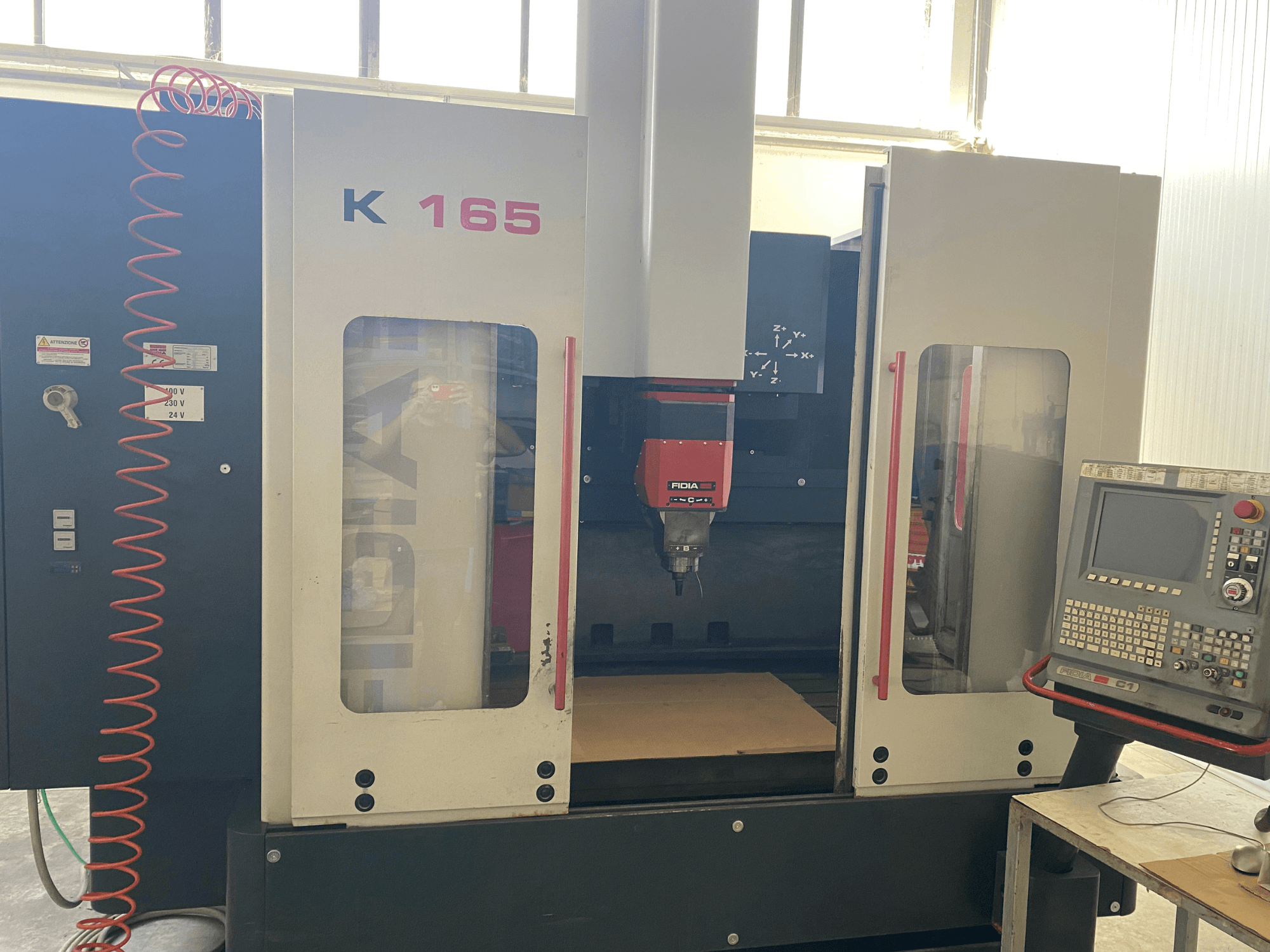 Stroj Fidia K 165 CNC s červeným vřetenem a ovládacím panelem, pohled zepředu, v dobře osvětlené dílně.