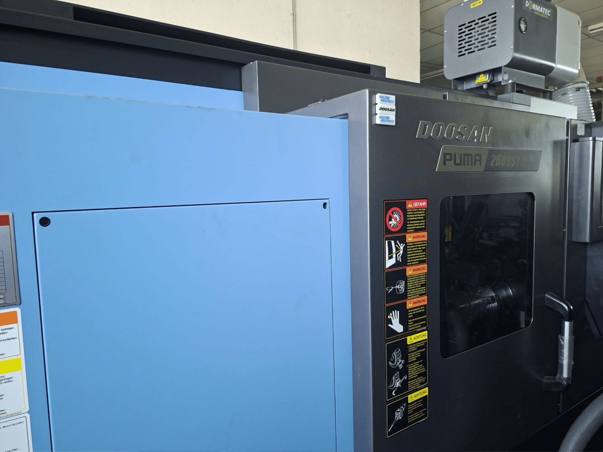 Horizontální soustruh DOOSAN PUMA 2600 SY II, pohled zepředu, bezpečnostní štítky a modré obložení.