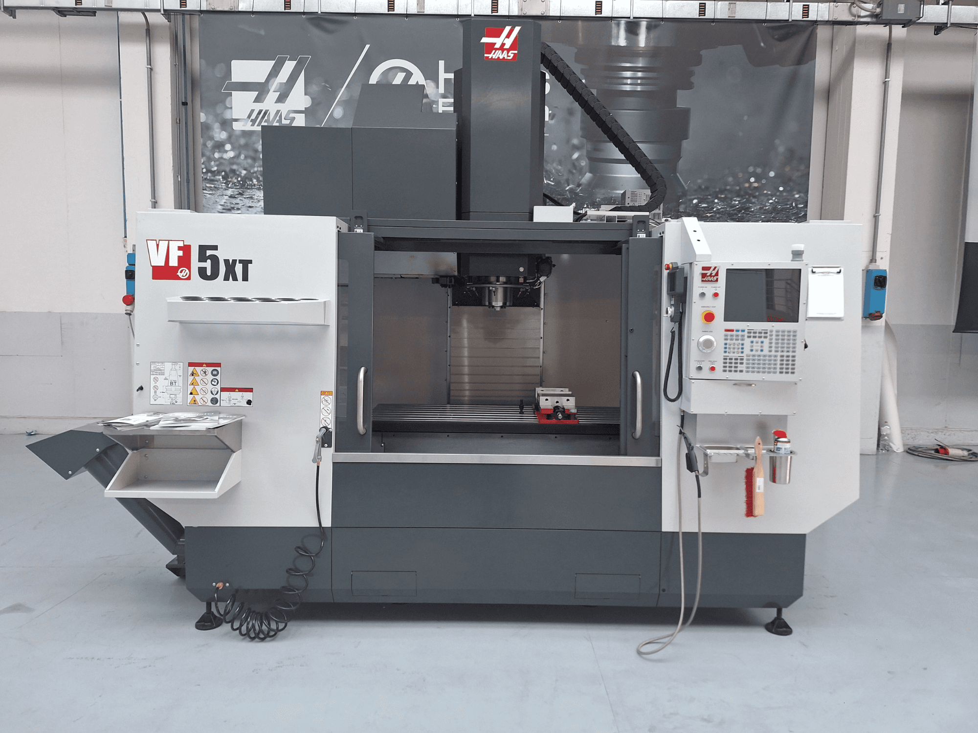 Vertikální obráběcí centrum HAAS VF-5/50XT, pohled zepředu, na kterém je vidět ovládací panel, oblast vřetena a úložný prostor pro nástroje.