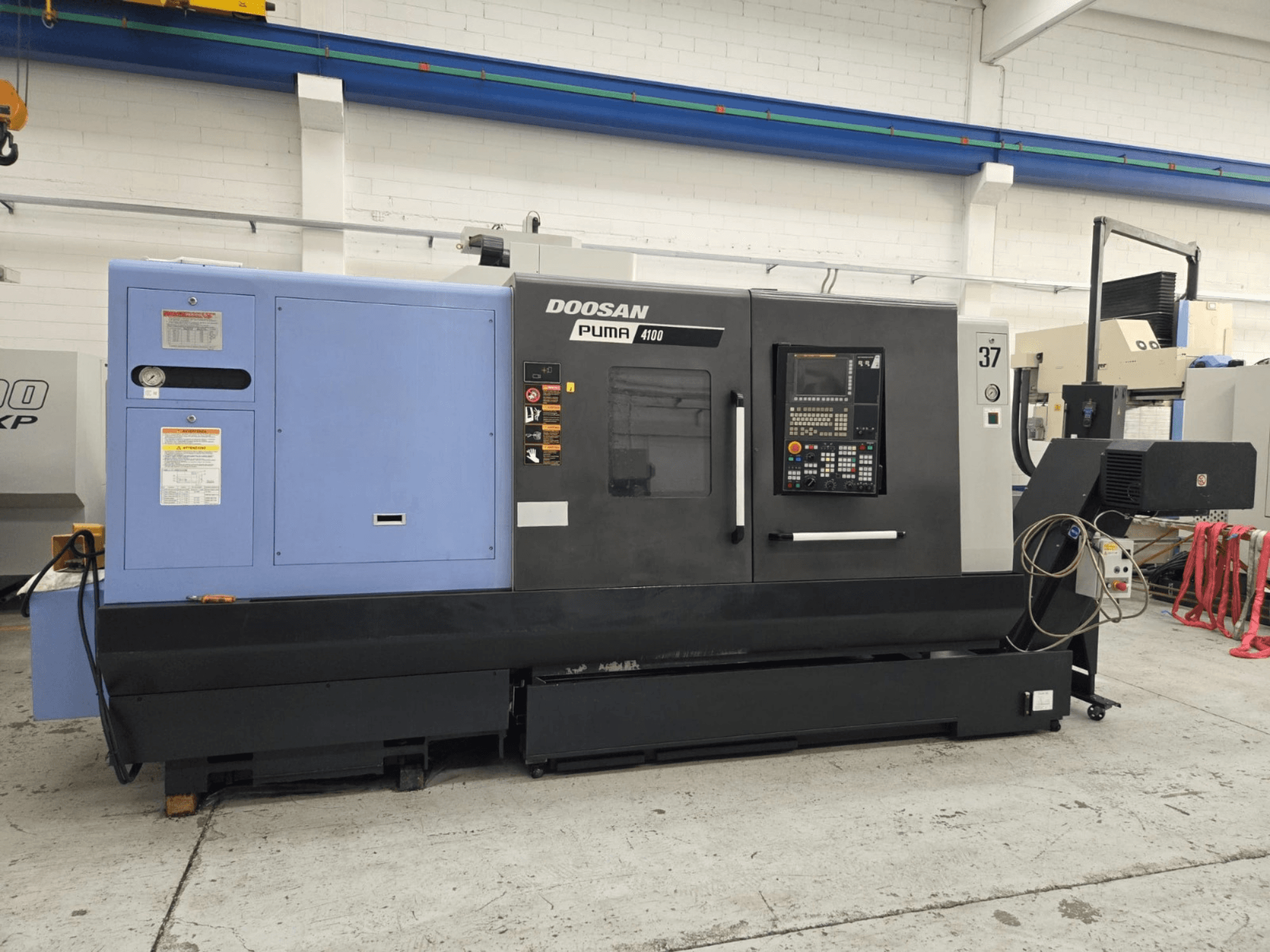 CNC soustruh Doosan Puma 4100, pohled zepředu; ovládací panel, modrá pohonná jednotka a podrobné popisky pro orientaci při práci.