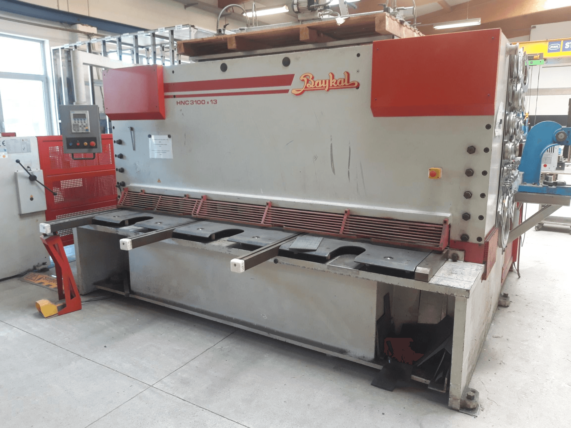 Čelní pohled na CNC nůžky Baykal HNC 3100x13 s ovládacím panelem, prostorem pro řezání kovu a prostorem pro sběr odpadu.