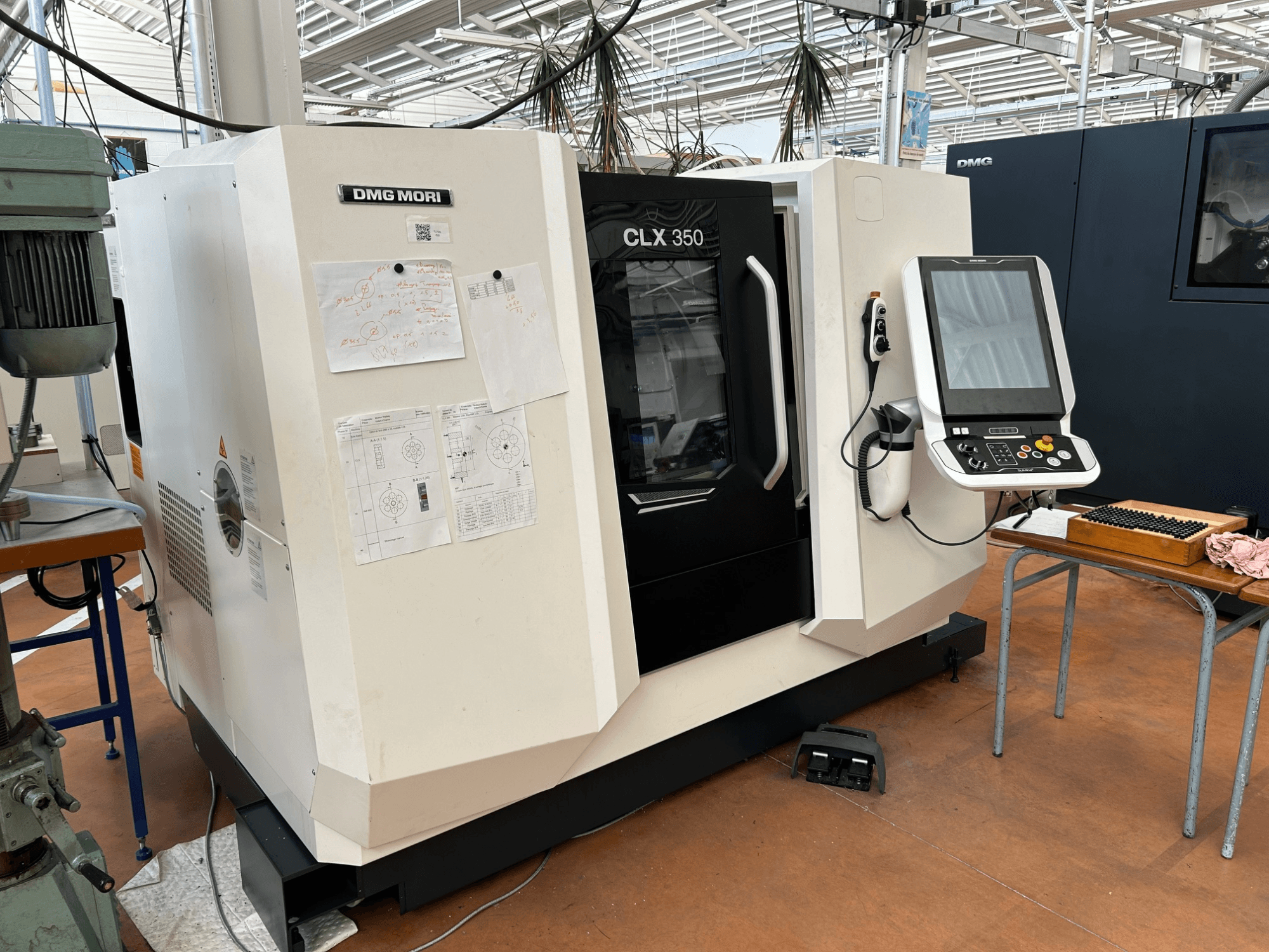 Horizontální soustruh DMG MORI CLX 350 V4, pohled zepředu s ovládacím panelem a přiloženou technickou dokumentací.