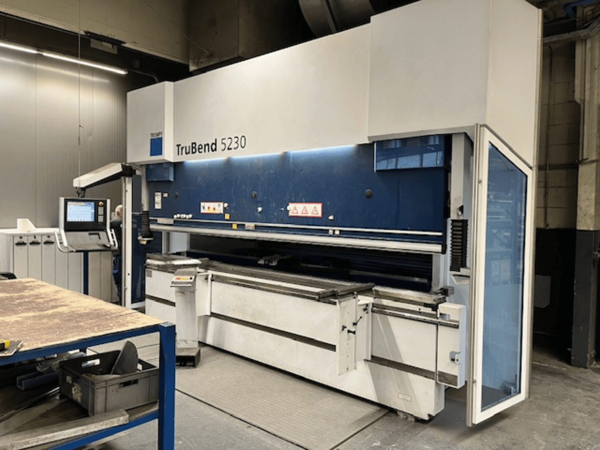 Ohýbačka TruBend 5230 v průmyslovém prostředí; pohled zepředu ukazuje ovládací panel, bezpečnostní prvky a pracovní stůl.