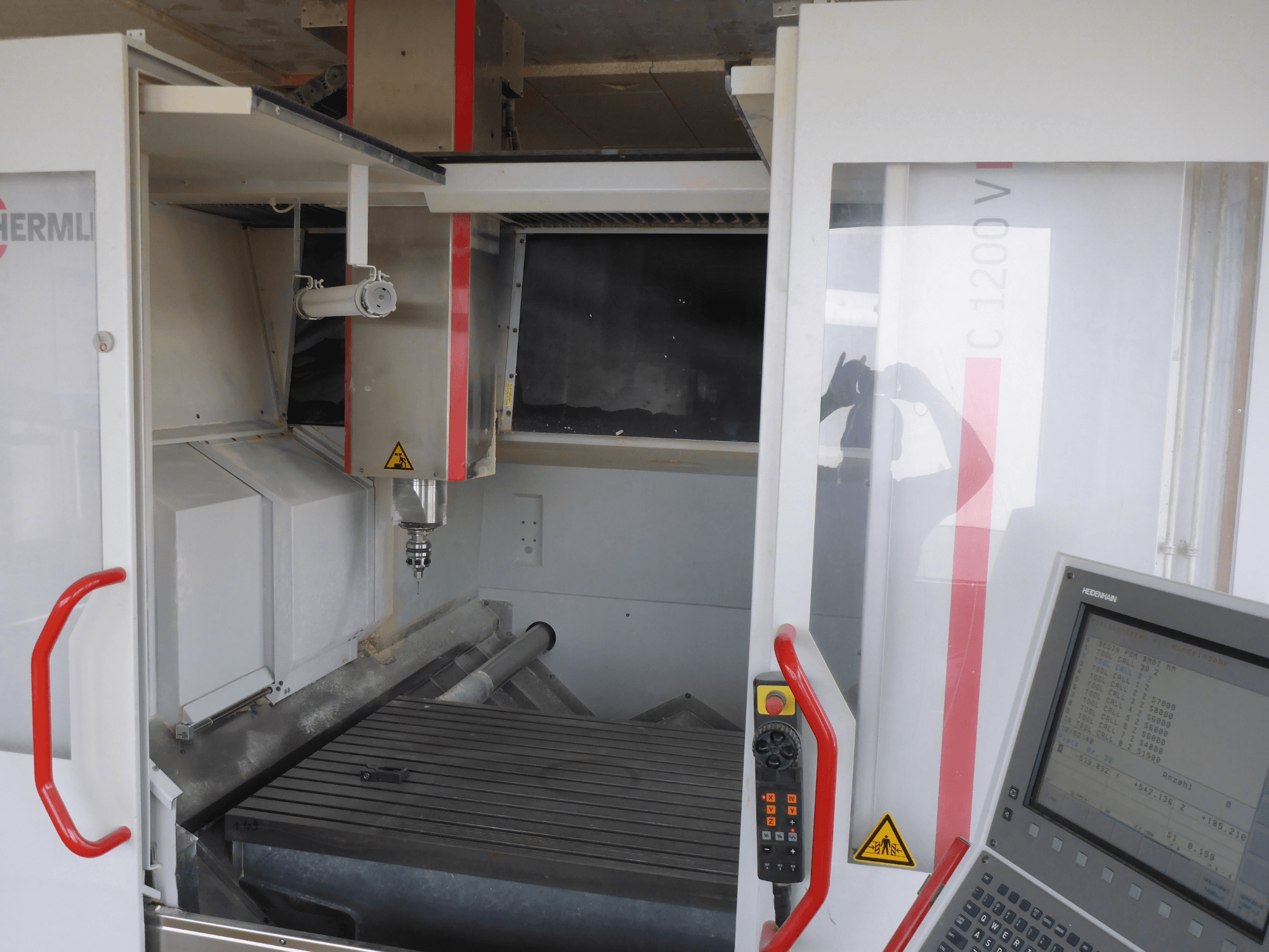 Interiér vertikálního obráběcího centra HERMLE C 1200 s držákem nástrojů, ovládacím panelem a pracovním stolem z čelního pohledu.