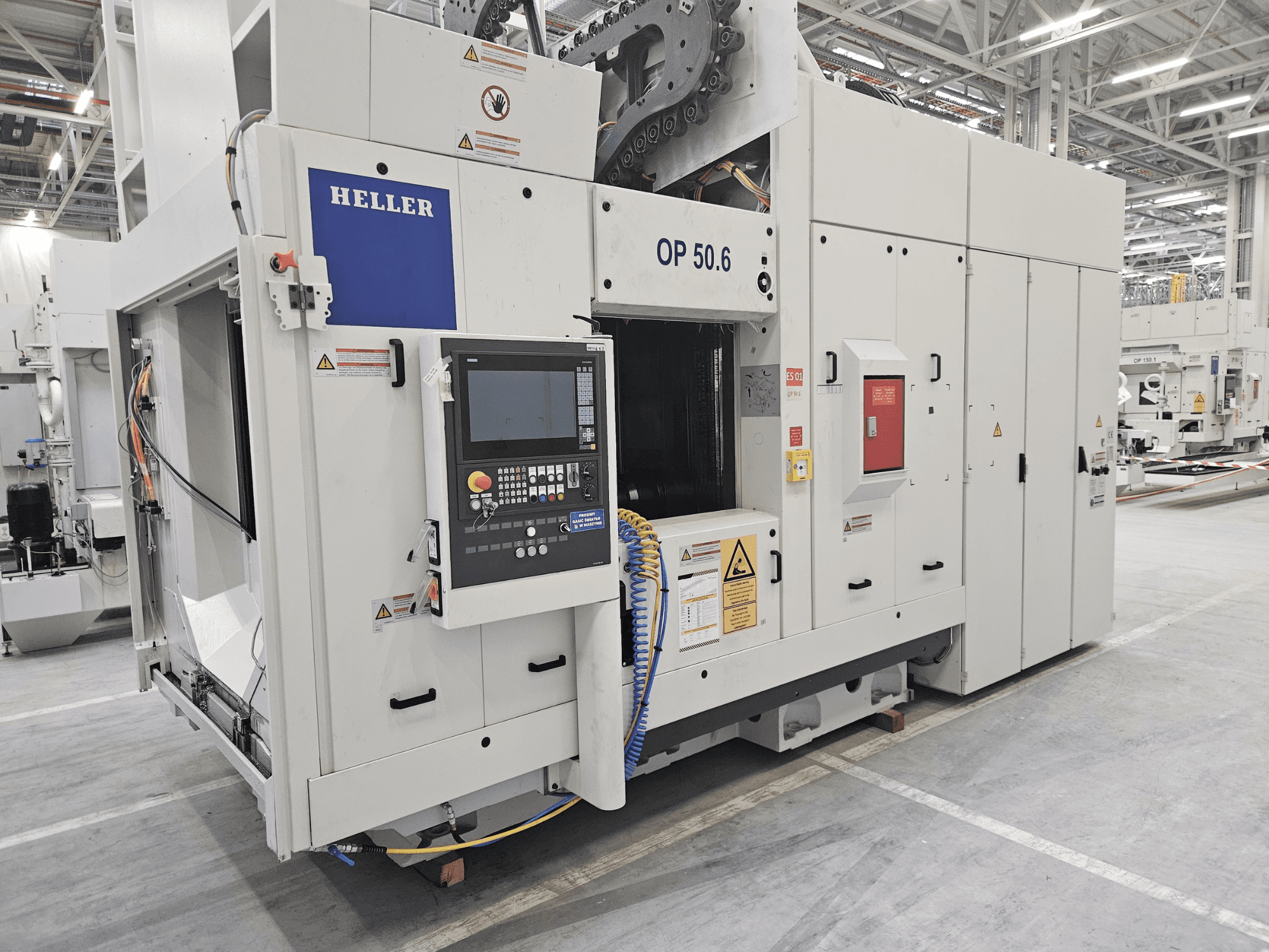 Obráběcí centrum Heller OP 50.6, pohled zepředu, s viditelným ovládacím panelem, výstražnými štítky a hadicemi v továrním prostředí.
