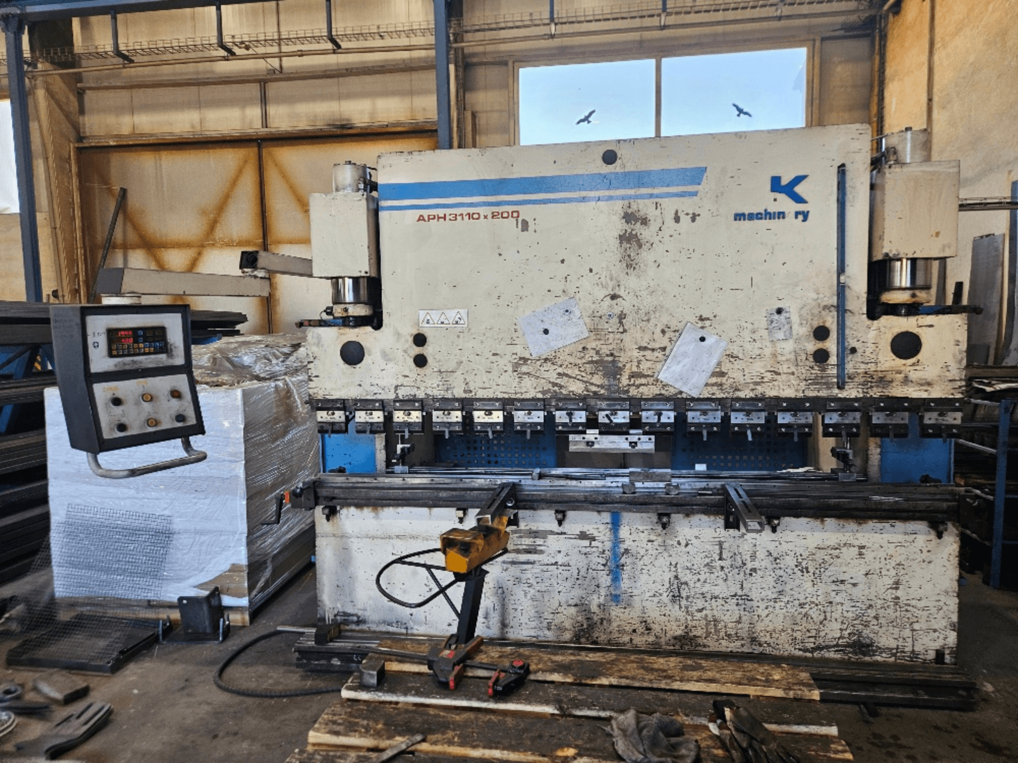 Ohraňovací lis Baykal APH 3110x200 v dílně, pohled zepředu, s viditelným ovládacím panelem, plechy a nástroji.