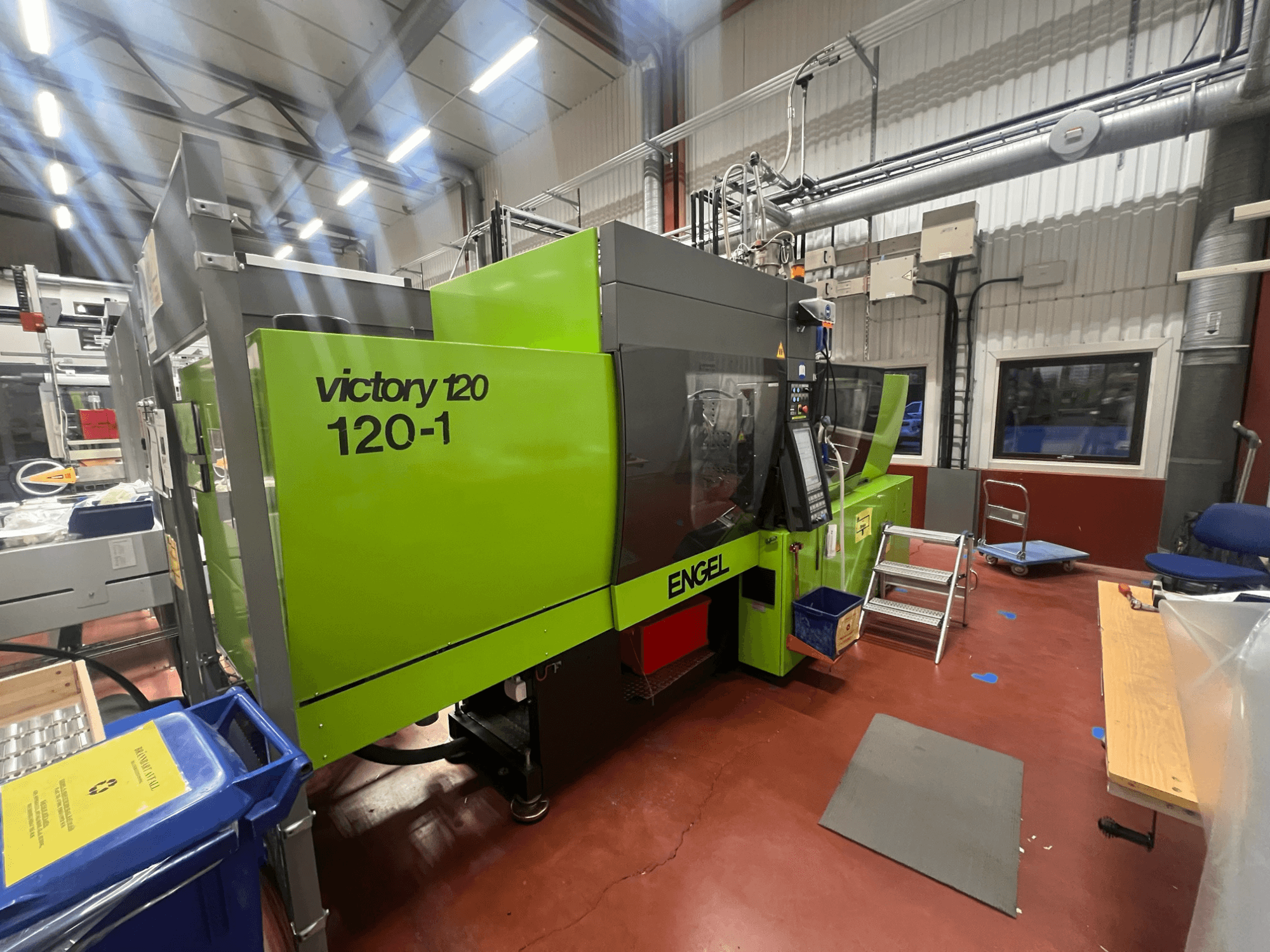 Zelený vstřikovací stroj ENGEL Victory 120-1, pohled zepředu, s ovládacím panelem a schůdky, v průmyslovém prostředí.