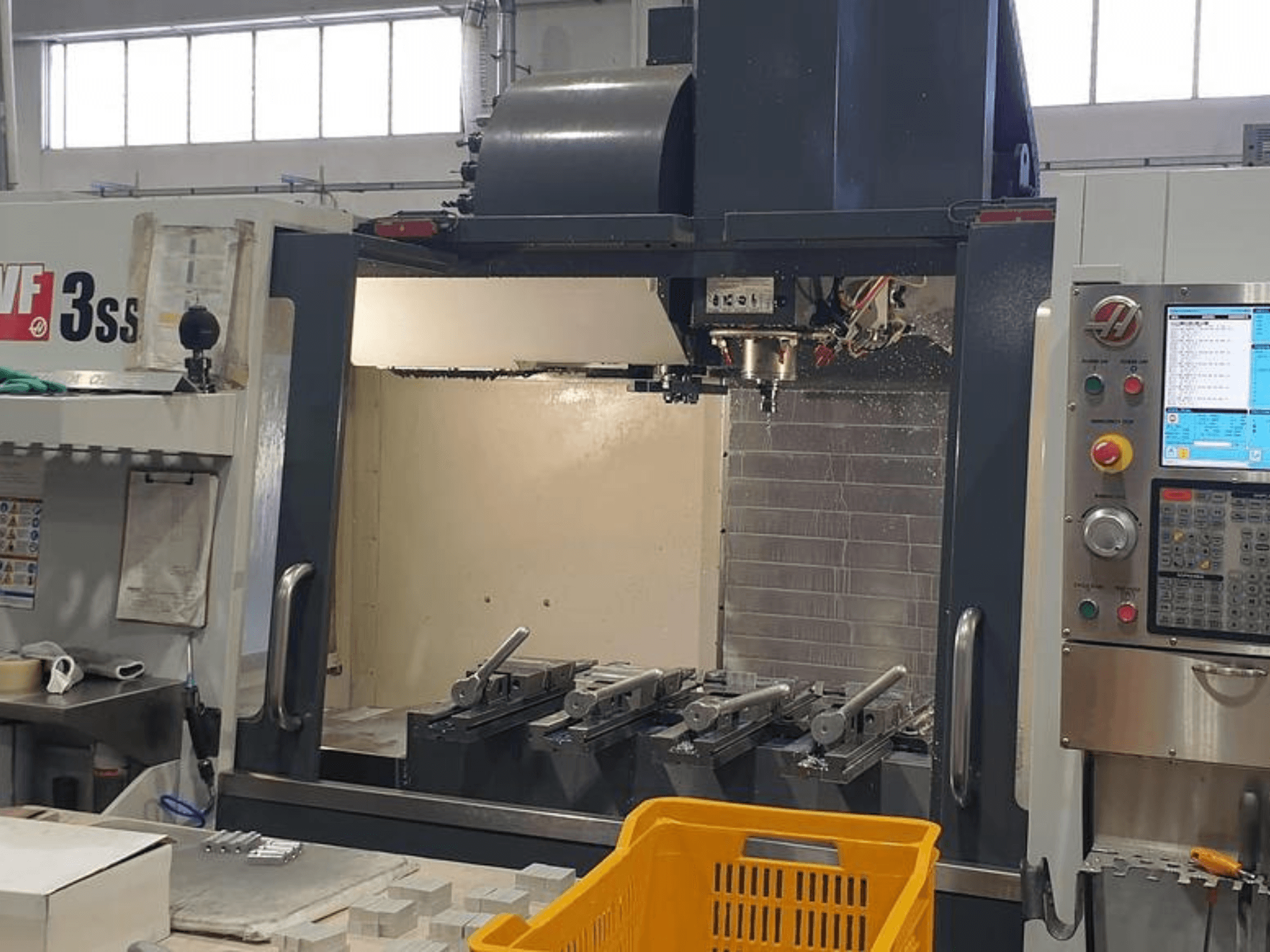 Vertikální obráběcí centrum HAAS VF-3SS, pohled zepředu s ovládacím panelem CNC, nástroji a oranžovým košem.