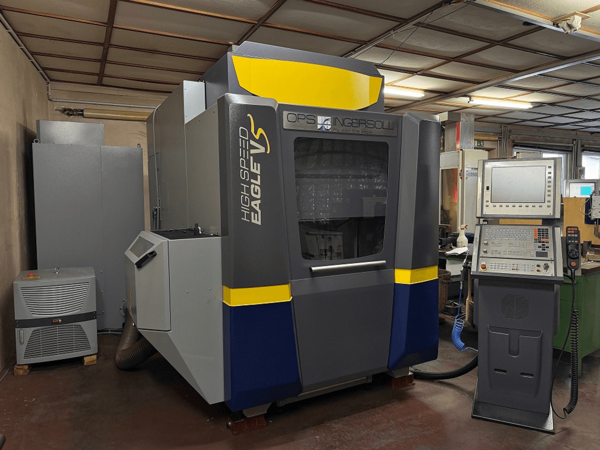 Vysokorychlostní stroj Eagle V od společnosti OPS Ingersoll, boční pohled, s ovládacím panelem a přilehlým vybavením v průmyslovém prostředí.