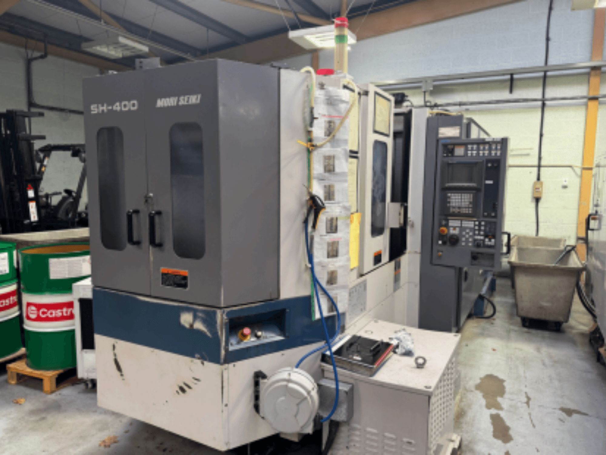 Stroj Moni Seiki SH-400 CNC, boční pohled zobrazující ovládací panel, dveře a okolní průmyslové prostředí.